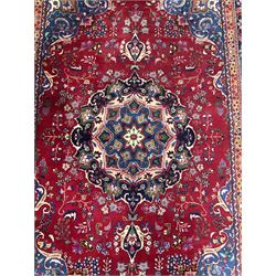 Persian Meshed red ground rug, central floral rosette medallion surrounded by trailing branch and stylised flower heads, repeating scrolling border