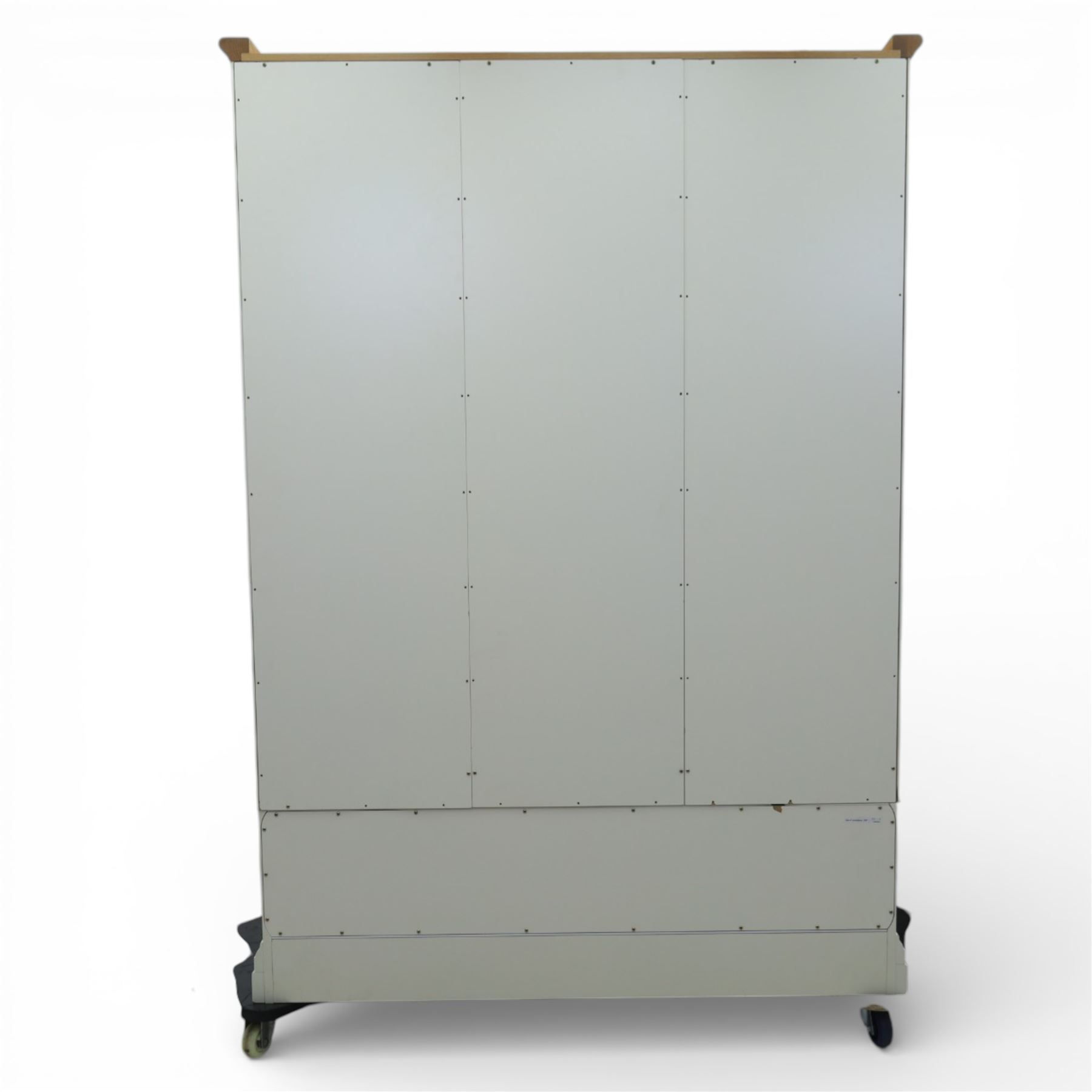 Modern triple wardrobe in white finish with oak moulded top enclosed by three doors with three drawers to base, with metal cup handles raised on bracket feet