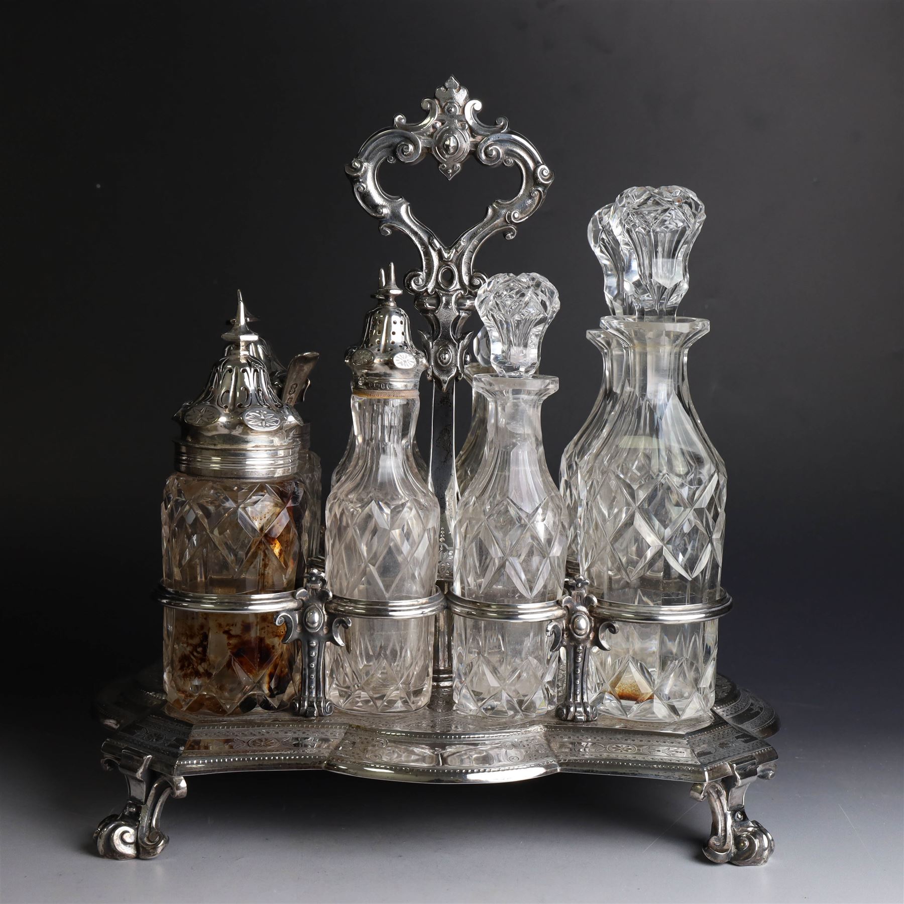 Victorian silver cruet stand, containing eight cut glass cruet bottles, four with silver covers, upon a shaped base with four scroll feet and loop handle, chased with floral and foliate decoration, the stand, base and bottle caps all hallmarked John, Edward, Walter & John Barnard, London 1872, one bottle with a matched silver cruet spoon, stand H30cm