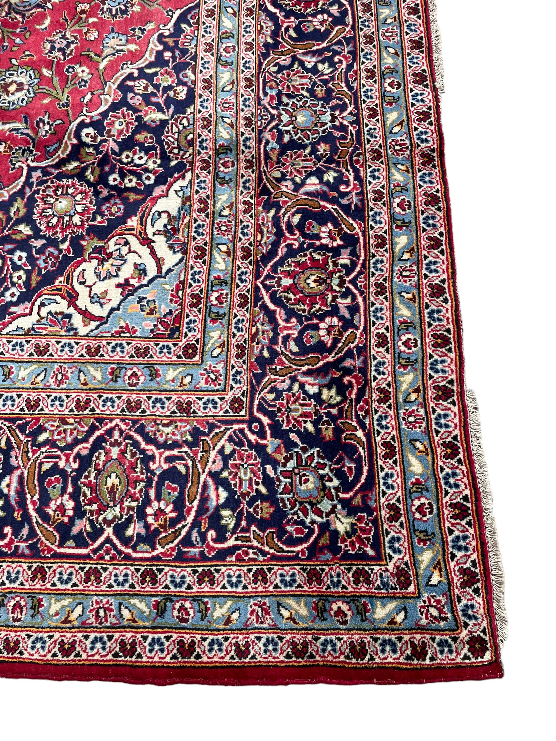 Central Persian Kashan crimson ground carpet, central  floral pole medallion with matching spandrels within a field of scrolling palmette motifs and foliage, the heavily banded indigo border with repeating plant motifs interlaced with scrolled branches