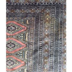Large Persian Bokhara wool rug, the field decorated with repeating gul motifs in lozenge medallions across a dark ground, enclosed by multiple geometric borders in indigo, ivory and terracotta, from the region of Baluchistan