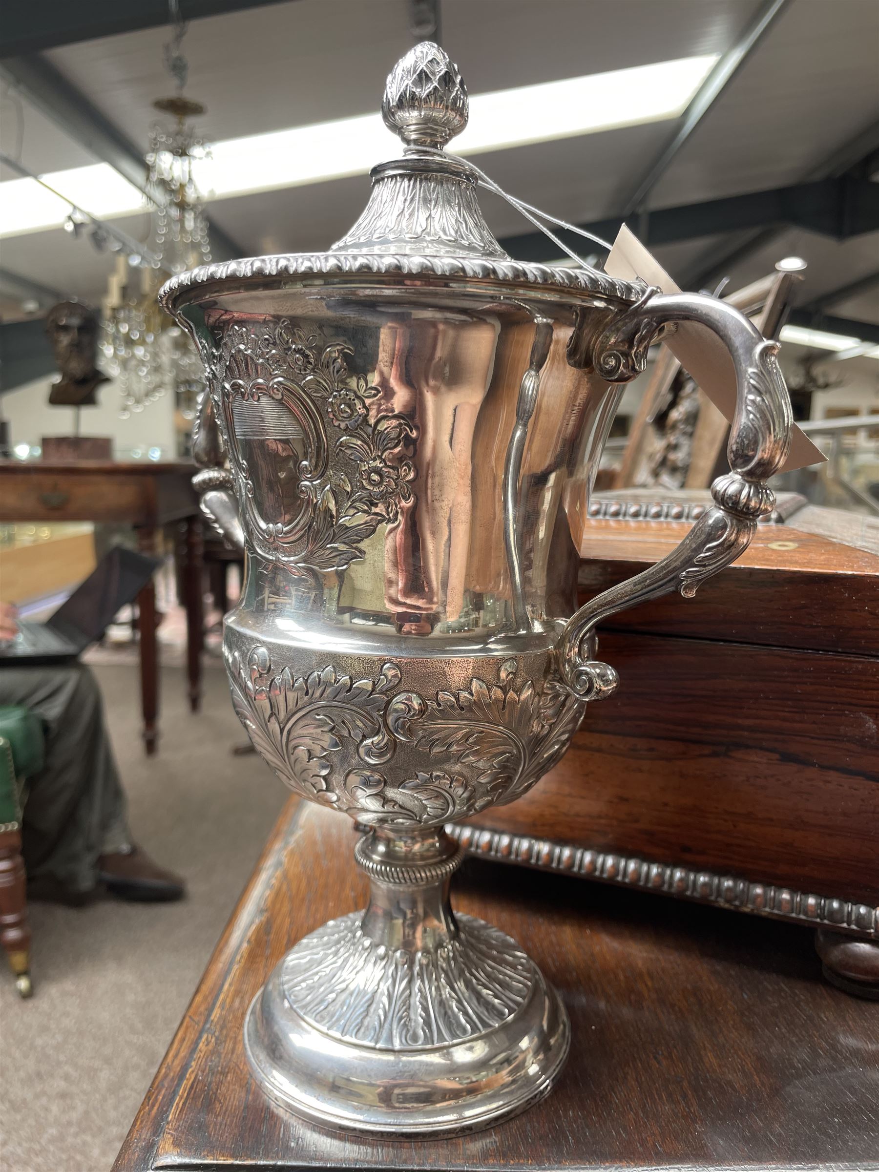 George III silver two handled campana shape cup and cover with pineapple lift, the body with cartouche surrounded by flowers above leaves and scrolls on a pedestal foot with acanthus leaf decoration H29cm London 1764, makers marks rubbed