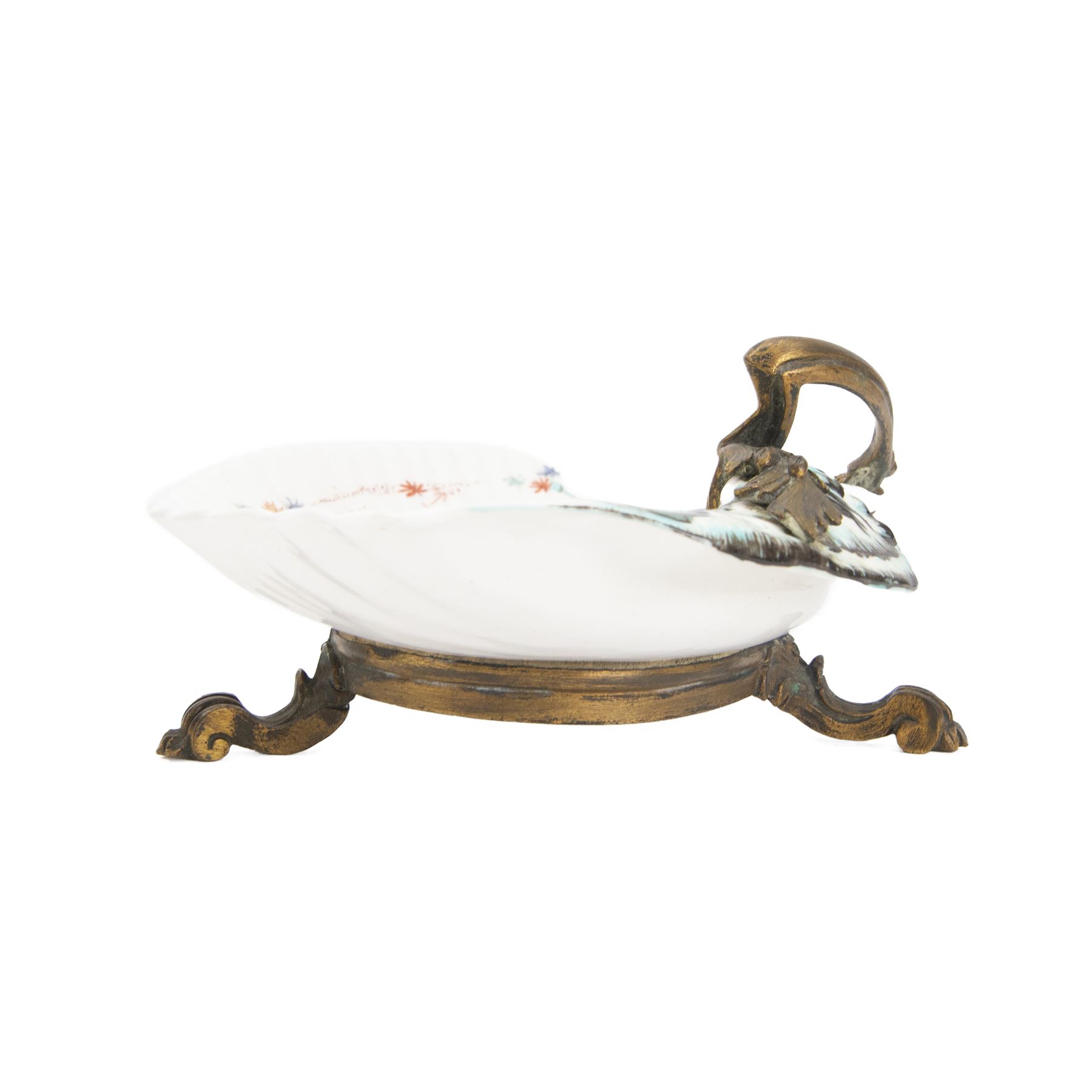 18th century porcelain dish, attributed to Chantilly, circa 1740-1750, with later ormolu mounted handle and feet, the dish of moulded shell form, painted in the Kakiemon pallet with an exotic bird and grasshopper amidst flowers and foliage, with foliate ormolu handle, and upon three scrolling foliate feet, possible obscure Chantilly mark beneath, including handle H10cm W31cm

A letter from the Ashmolean Museum accompanied the dish when it entered the current vendor's family collection. In the letter, Dr. Impey noted that the painting is European, possibly Dutch. The general consensus was that the shell dates to the 18th century, with the ormolu mounts likely added in the 19th century. However, the factory of origin remained unidentified. The letter was signed by Ian Lowe in 1974. Further consultation at the time with four members of staff at the Victoria and Albert Museum yielded differing opinions, with suggestions including Chantilly and Bow. The piece has been attributed to Chantilly partly due to what appears to be a partially obliterated horn motif beneath.