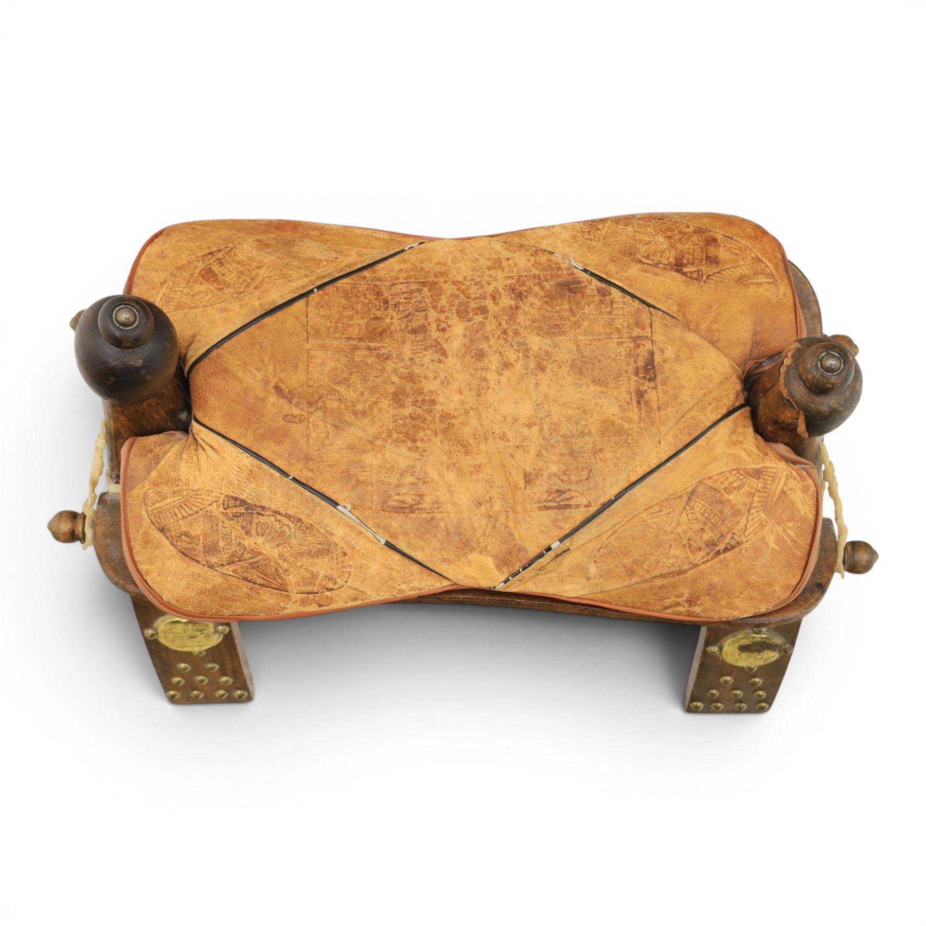 20th century Camel stool, with wooden turned finials, above a tooled leather seat, curved supports with brass applications 