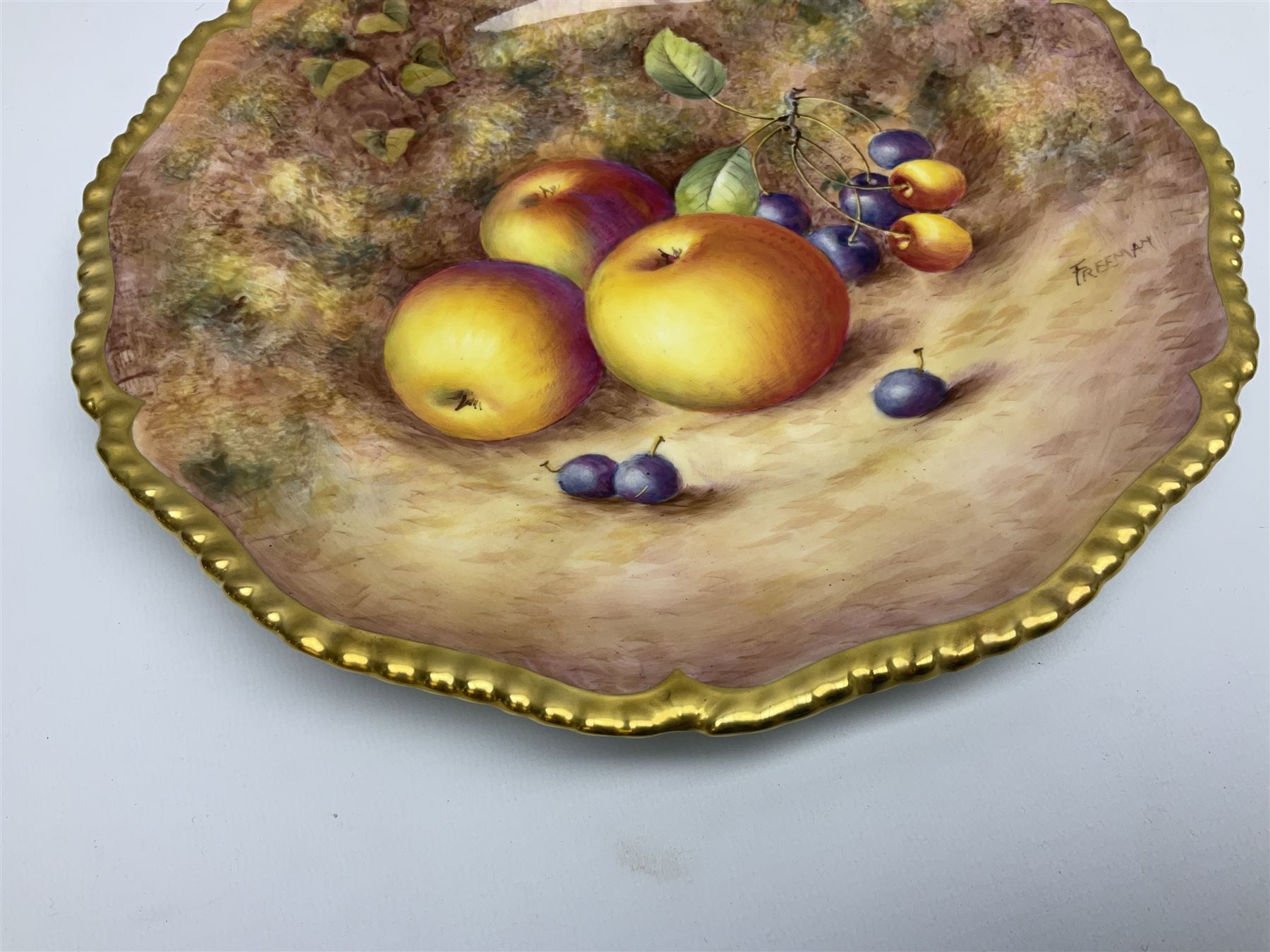 Mid 20th century Royal Worcester cabinet plate decorated by John Freeman, of circular form with gilt shaped rim, hand painted with a still life of fruit upon a mossy ground, signed Freeman, with black printed mark beneath, D27cm