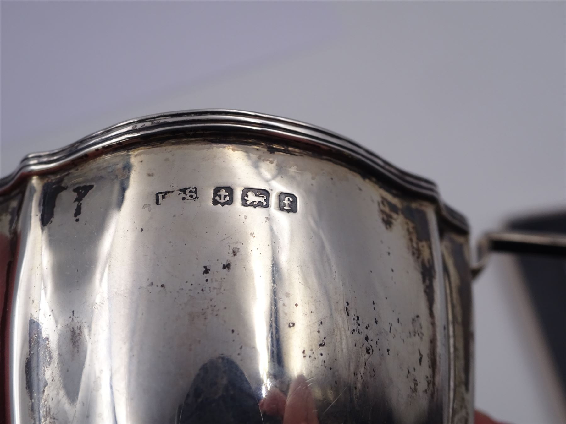 Edwardian silver cream jug, of fluted helmet form, with angular handle and upon shaped foot, hallmarked Birmingham 1905, maker's mark indistinct, together with a set of six Edwardian silver teaspoons and a pair of sugar tongs, all with scrolling embossed decoration and engraved monogram, hallmarked Joseph Rodgers & Sons, Sheffield 1903, within tooled leather fitted case, jug including handle H9cm 