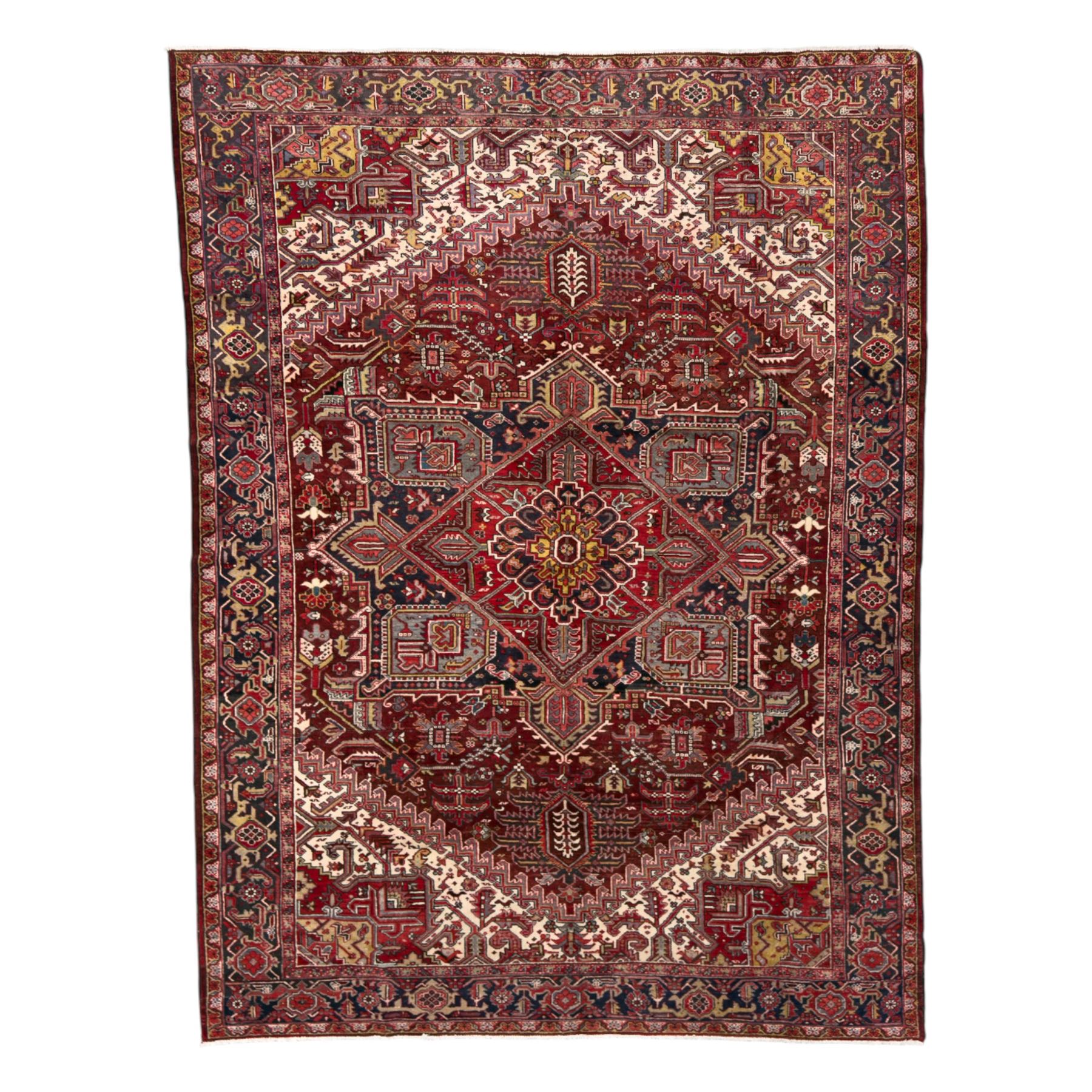 Northwestern Persian Heriz carpet, the madder red field centred by a large octofoil medallion with serrated edge, flanked by ivory stepped spandrels and geometric floral motifs in indigo, ochre and sky blue, enclosed by a navy border of rosettes and angular vines, from the region of Heriz