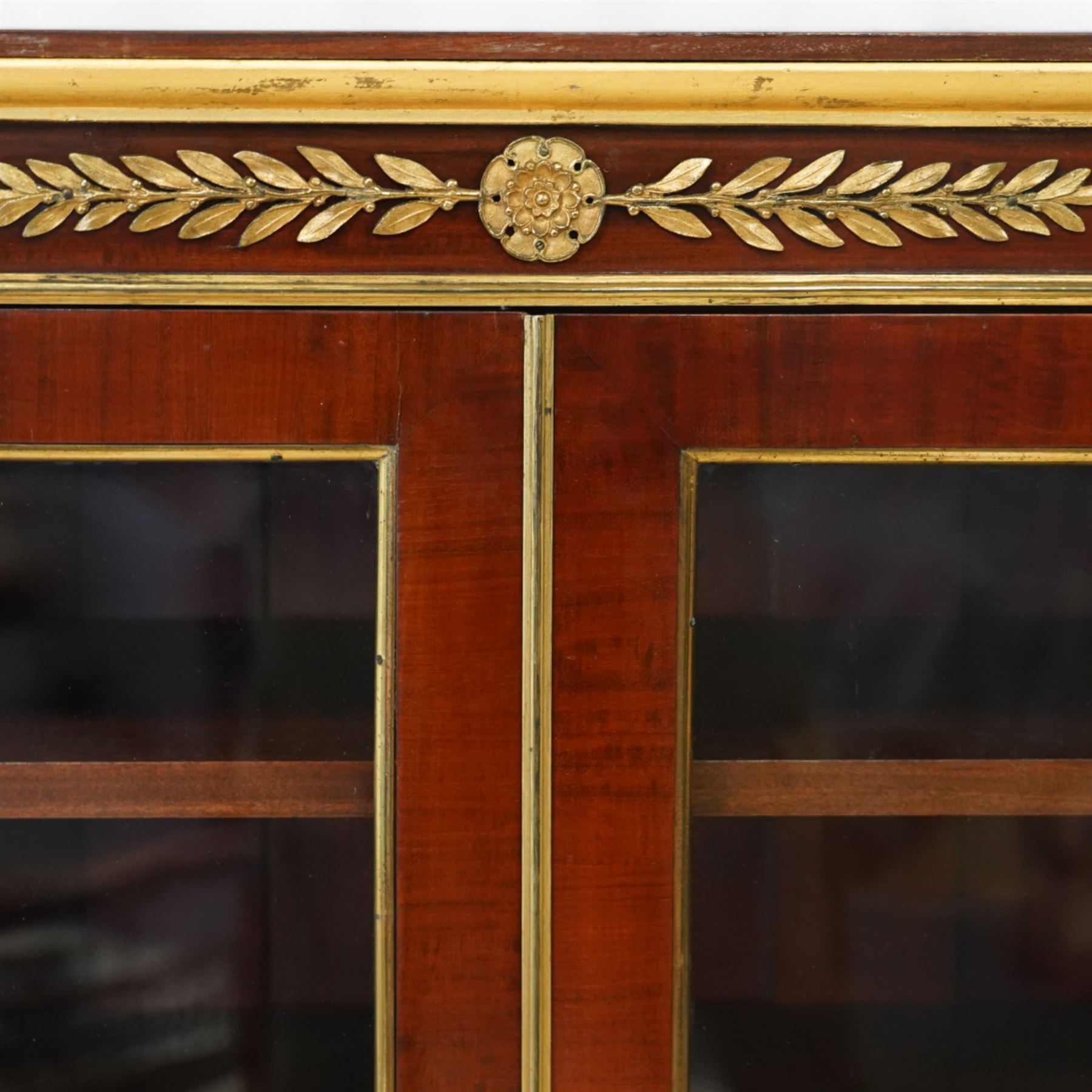 19th-century French Empire-style mahogany and gilt bronze-mounted glazed cabinet, rectangular top above frieze with applied gilt bronze laurel swags and rosettes with gilt brass borders, over two glazed panel doors enclosing three adjustable shelves, flanked by plain pilasters with applied mounts, raised on gilt bronze paw feet 