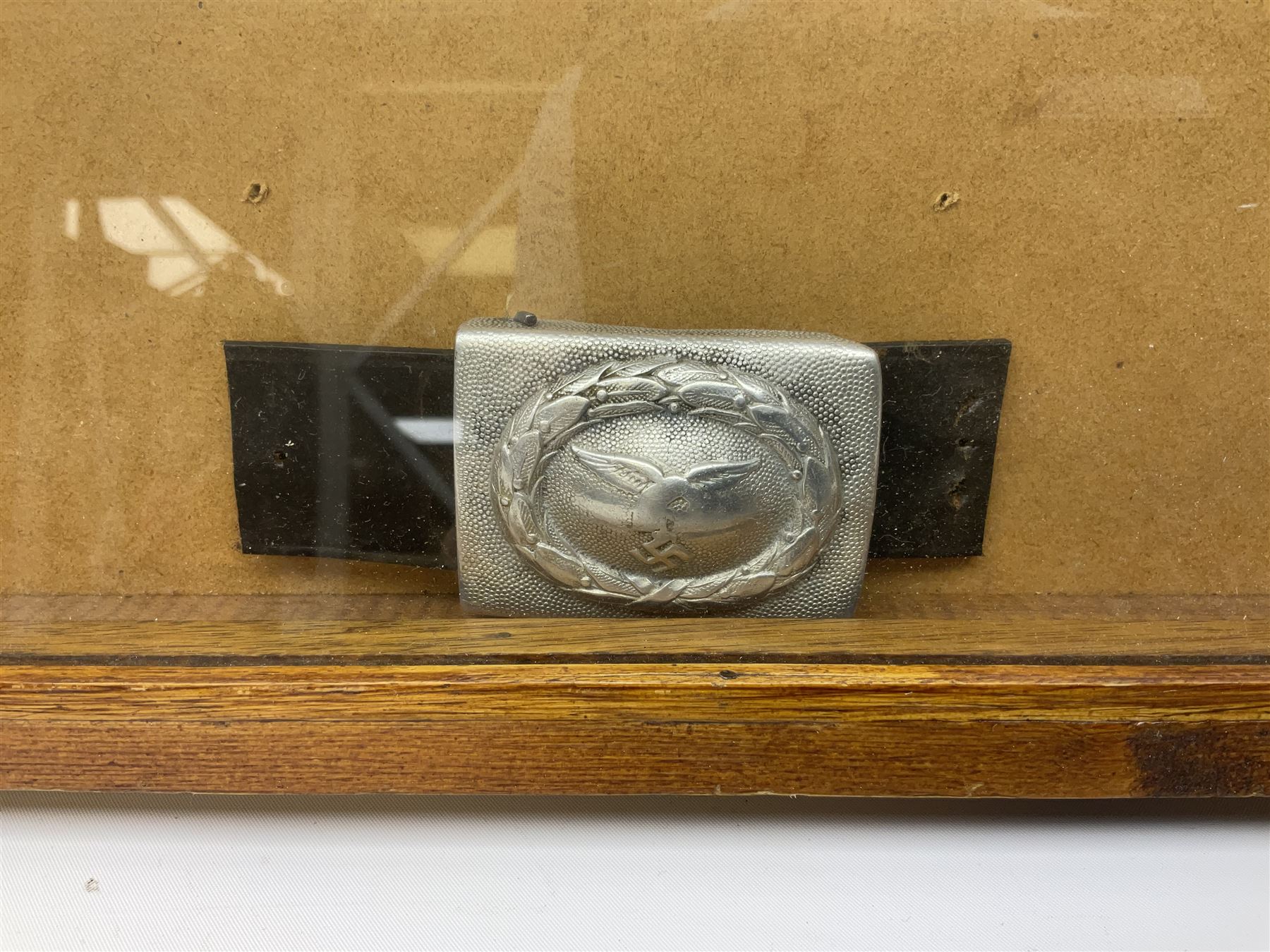 Display of eleven German belt buckles including 'SS', Party Buckle, two Army, Fire Service, two Luftwaffe, NSKK, Hitler Youth and WW1 Army; framed with three cloth badges and an armband