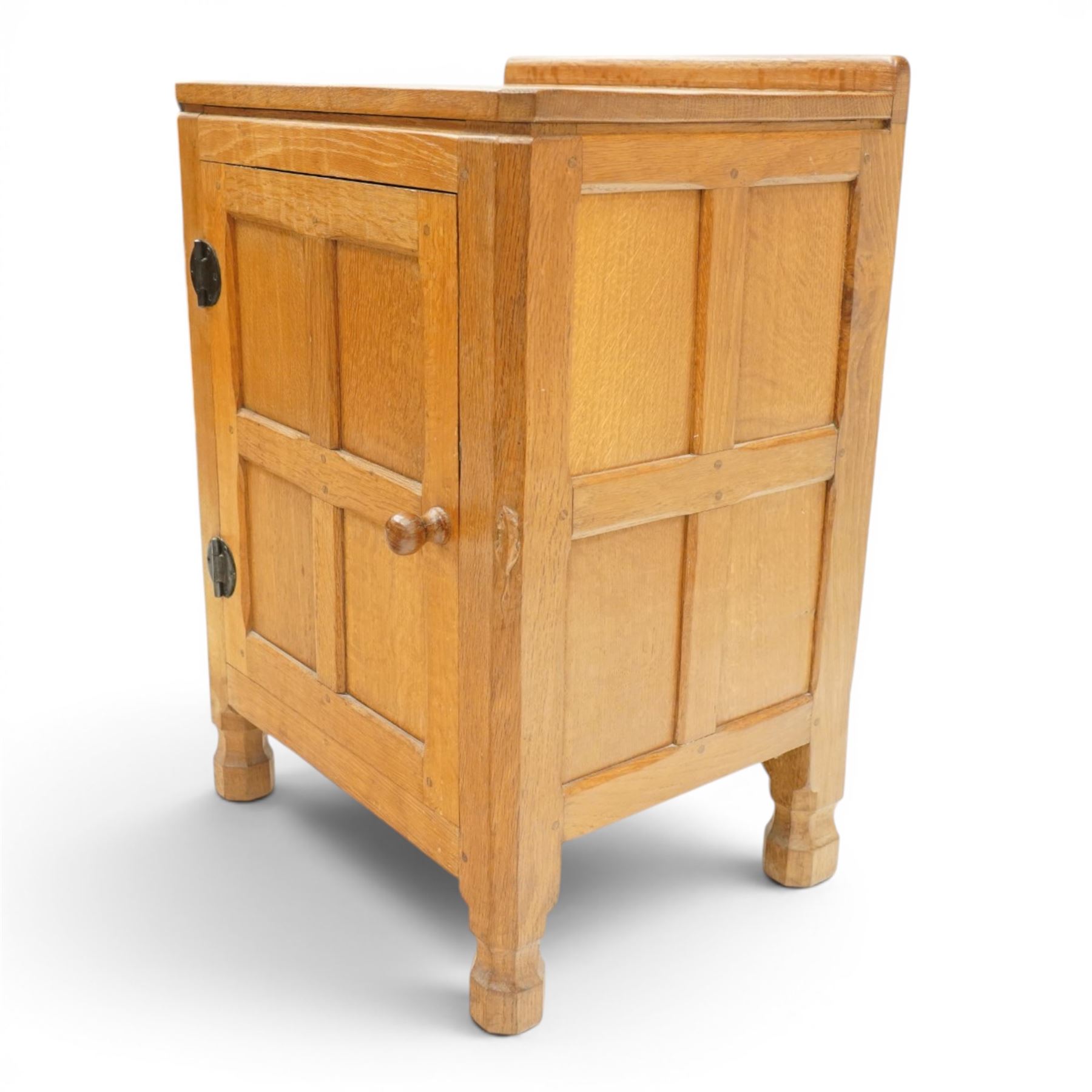 Mouseman - adzed and panelled oak bedside cupboard of small proportions, raised back over rectangular canted top, fitted with single panelled cupboard door with chamfered rails and turned knob handle, enclosing single shelf, raised on octagonal feet,  carved with mouse signature, by the workshop of Robert Thompson of Kilburn