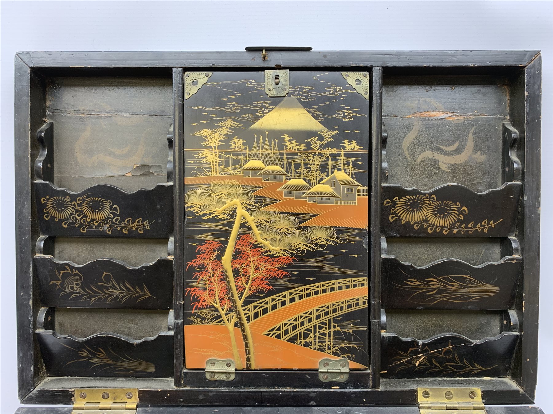  A 20th century Chinese black lacquer and gilt detailed writing box, decorated with figures, pagodas and cranes amidst a mountainous landscape, the hinged cover opening to reveal a compartmented interior and fold out baize lined slope, H20cm L46.5cm D31.5cm.   
