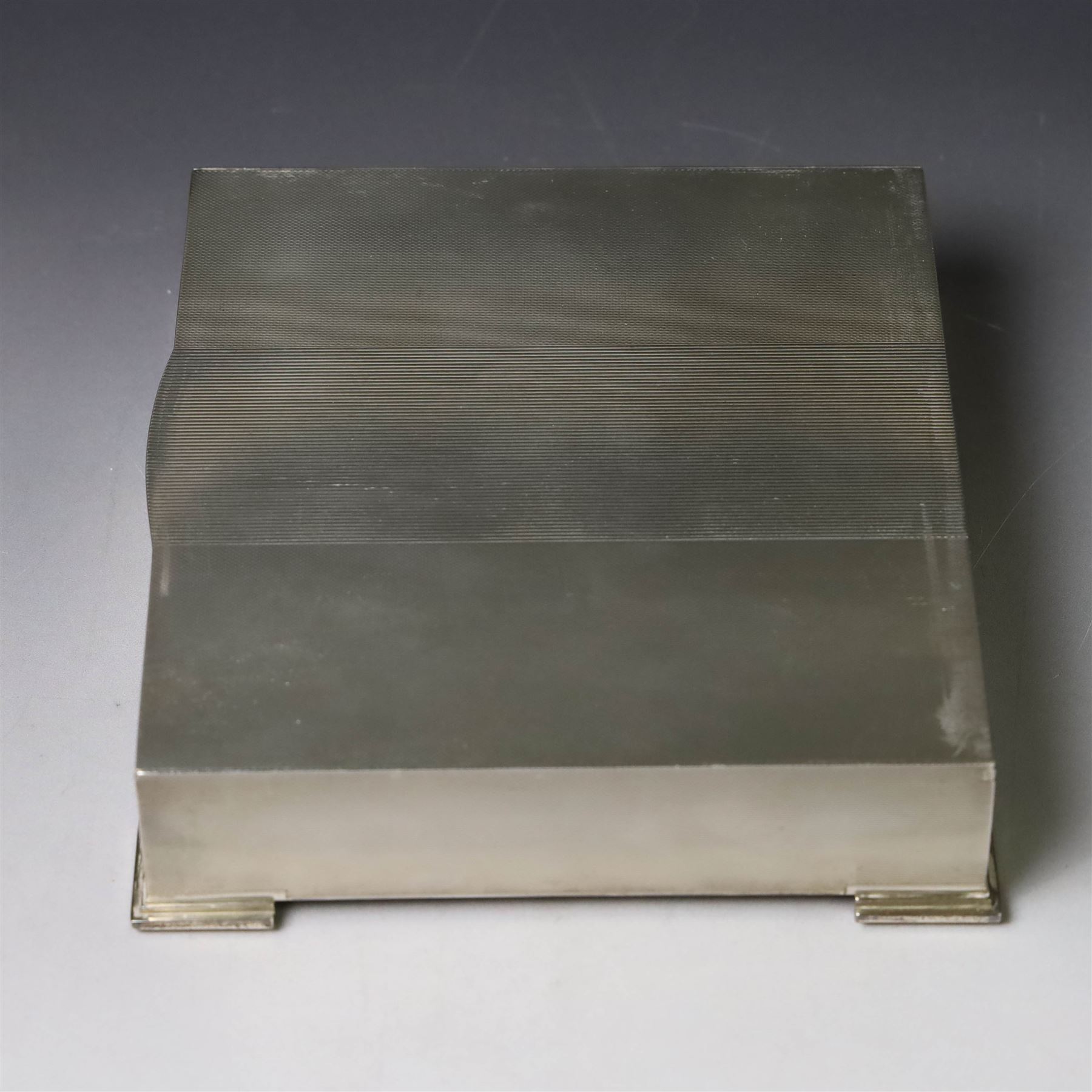 1960s silver mounted cigarette box, of rectangular form with engine turned decoration, upon four bracket feet, with presentation engraving to interior lid reading  'British Aircraft Corporation (Operating) Limited Commemorating the Queen's Award to Industry 1967, hallmarked James Geraghty, Birmingham 1965, with retailers mark for Asprey, W16.5cm, H4.5cm, in Garrard & Co Jewellers box
