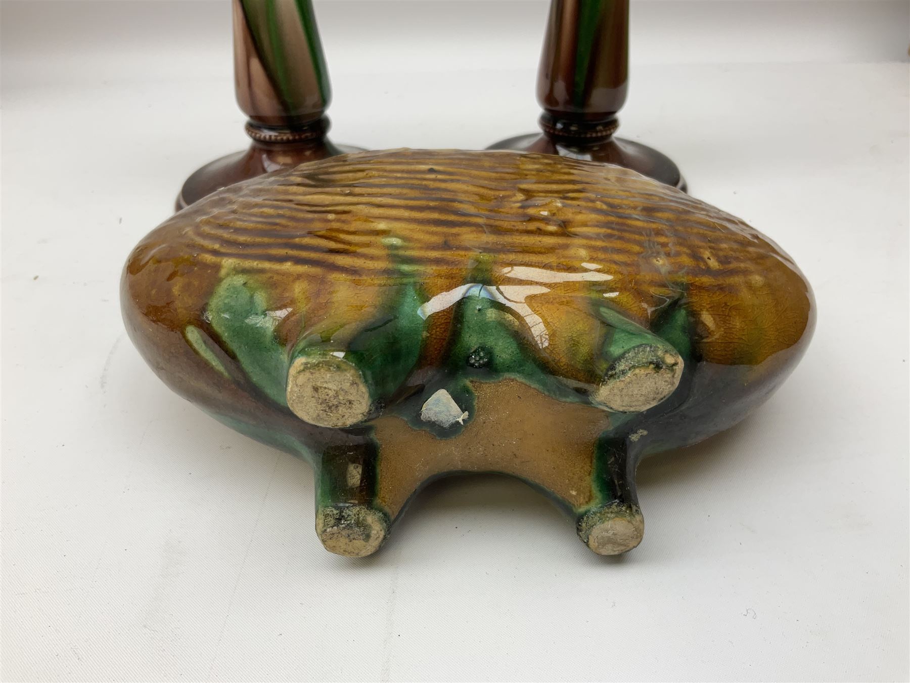 Linthorpe pottery vase with crimped rim and ovoid body, Linthorpe jug with high loop handle and crimped spout, a pair of candlesticks with a green, brown glaze and other similar pottery 