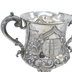 Victorian silver twin handled trophy, the bowl embossed with floral and scrolling decoration, with presentation engraving to body and twin acanthus capped C scroll handles, upon a lobed foot, hallmarked London 1866, maker's mark AM probably for Alexander Macrae, upon an ebonised wooden plinth, trophy only H25.5cm