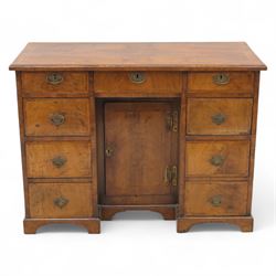 Early 20th-century Georgian-style walnut kneehole desk, the rectangular top with feather cross-banded border, above an arrangement of eight short drawers flanking a central cupboard door, fitted with brass backplate handles, raised on bracket feet