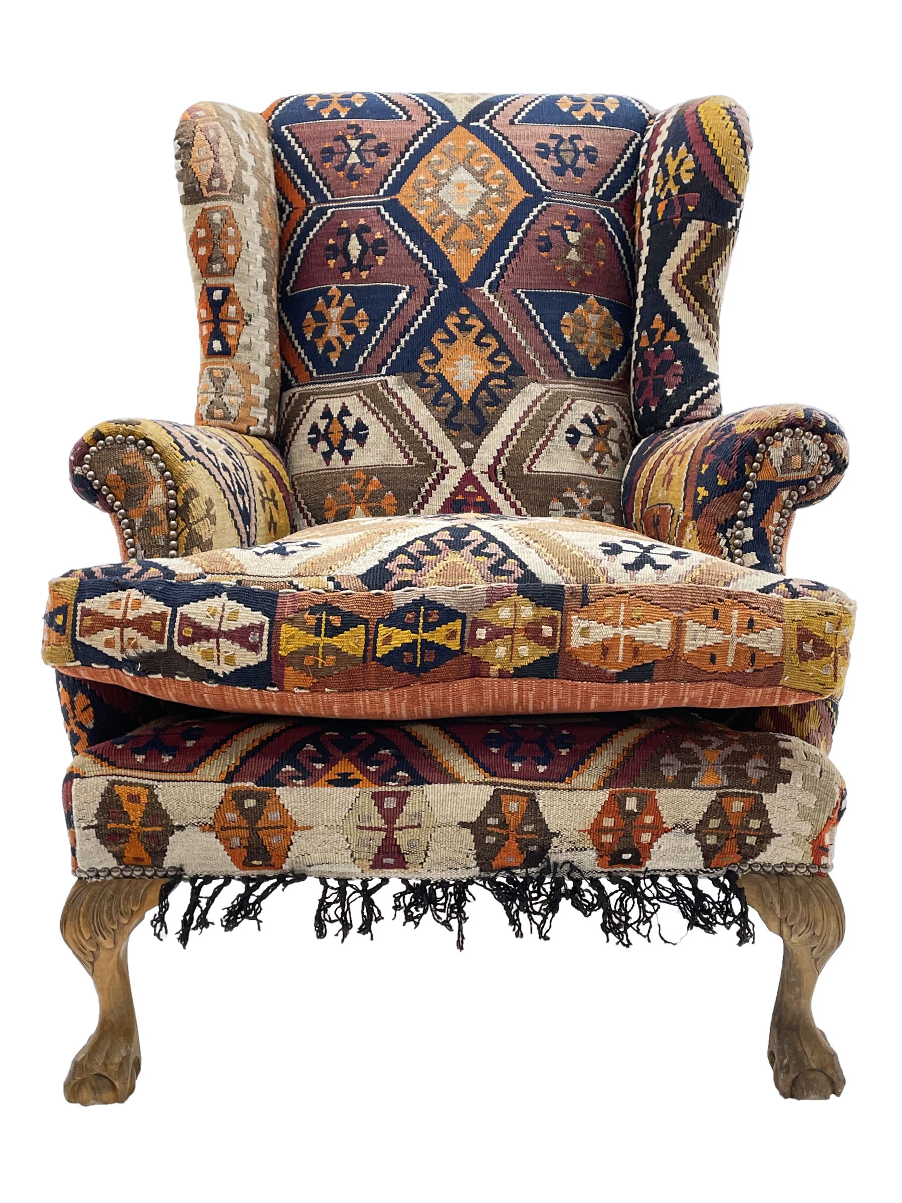 Late 20th century beech framed wingback armchair, sprung seat and back upholstered in kilim cover, acanthus carved cabriole supports with ball and claw feet