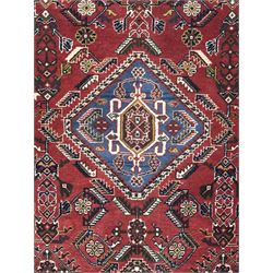 Persian Qashqai crimson ground runner, the central field decorated with three large geometric medallions with intricate angular and floral motifs, the indigo spandrels with complementary geometric designs, bordered by an ivory band with repeating floral patterns and angular vines