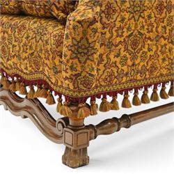 Pair of William & Mary design wingback armchairs, the arched high-back over rolled arms with a loose seat cushion and sprung seat, upholstered in old-gold ground foliate patterned fabric, raise on scroll feet united by a front serpentine stretcher