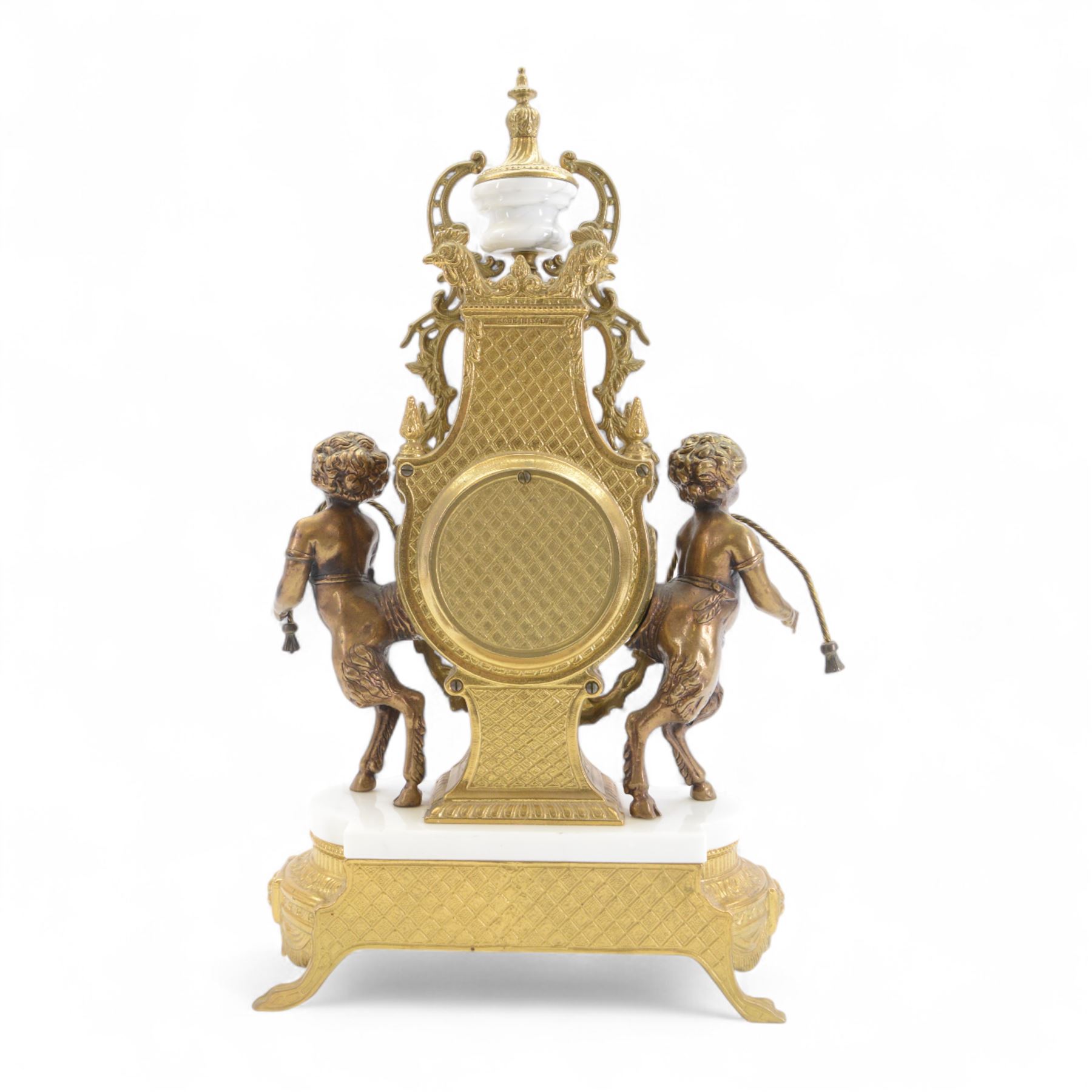 Italian- 20th century 8-day gilt figural mantle clock in the style of a 19th century Parisian lyre clock, drum movement with a porcelain dial flanked by playful cloven-hoofed cherubs on a white marble plinth, raised on a a decorative base with splayed paw feet, twin train spring driven Hermle movement with a floating balance escapement, sounding the hours and half hours on two bells. With key.    