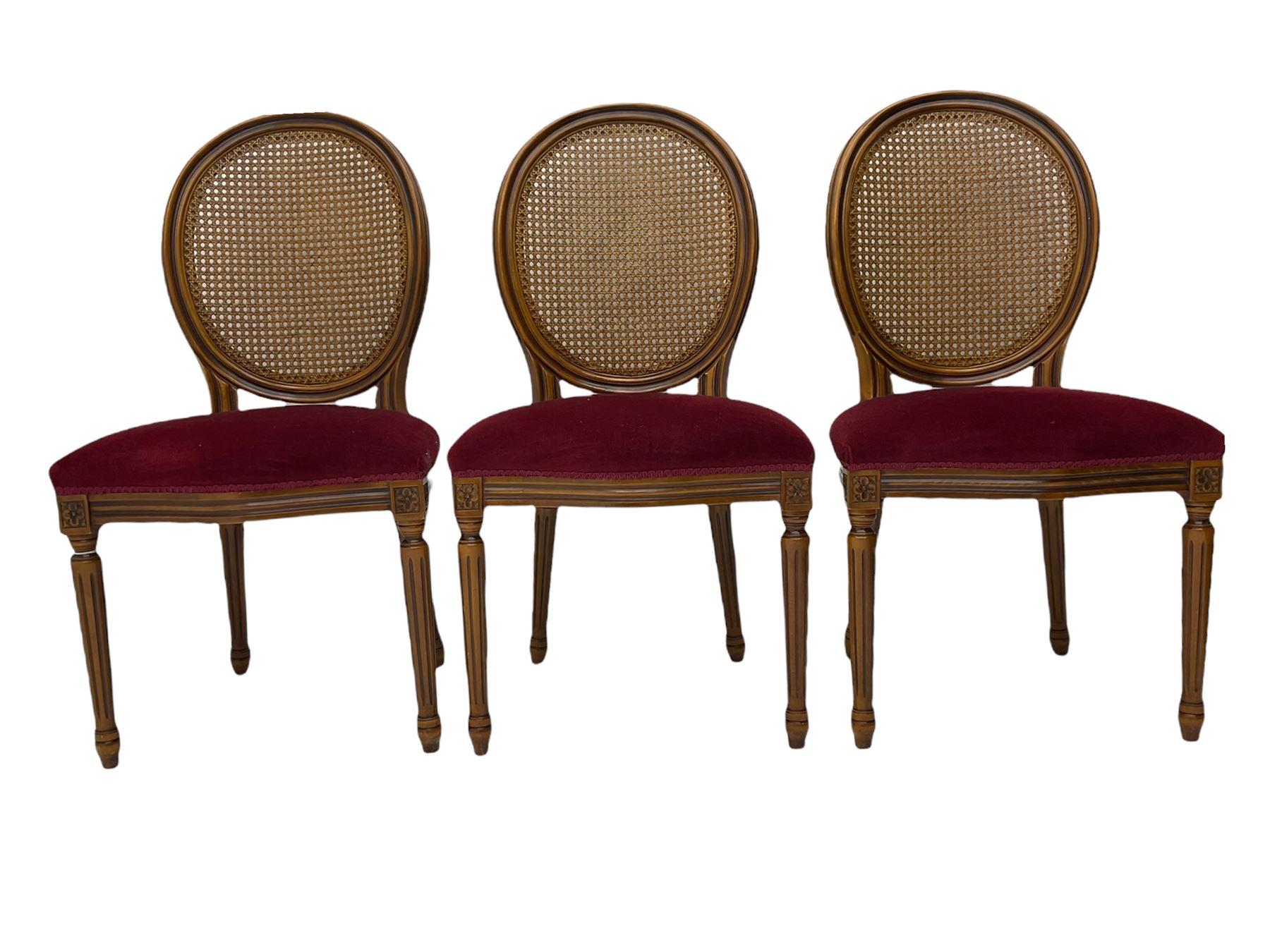 Set six French style walnut finish dining chairs, oval cane bergere backs over serpentine seats upholstered in red, flower head carved fluted supports
