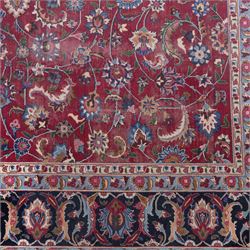 Persian Mashad design wool carpet, the red ground with dense scrolling floral and foliate decoration, within dark blue main border decorated with repeating palmettes and shaped leaves