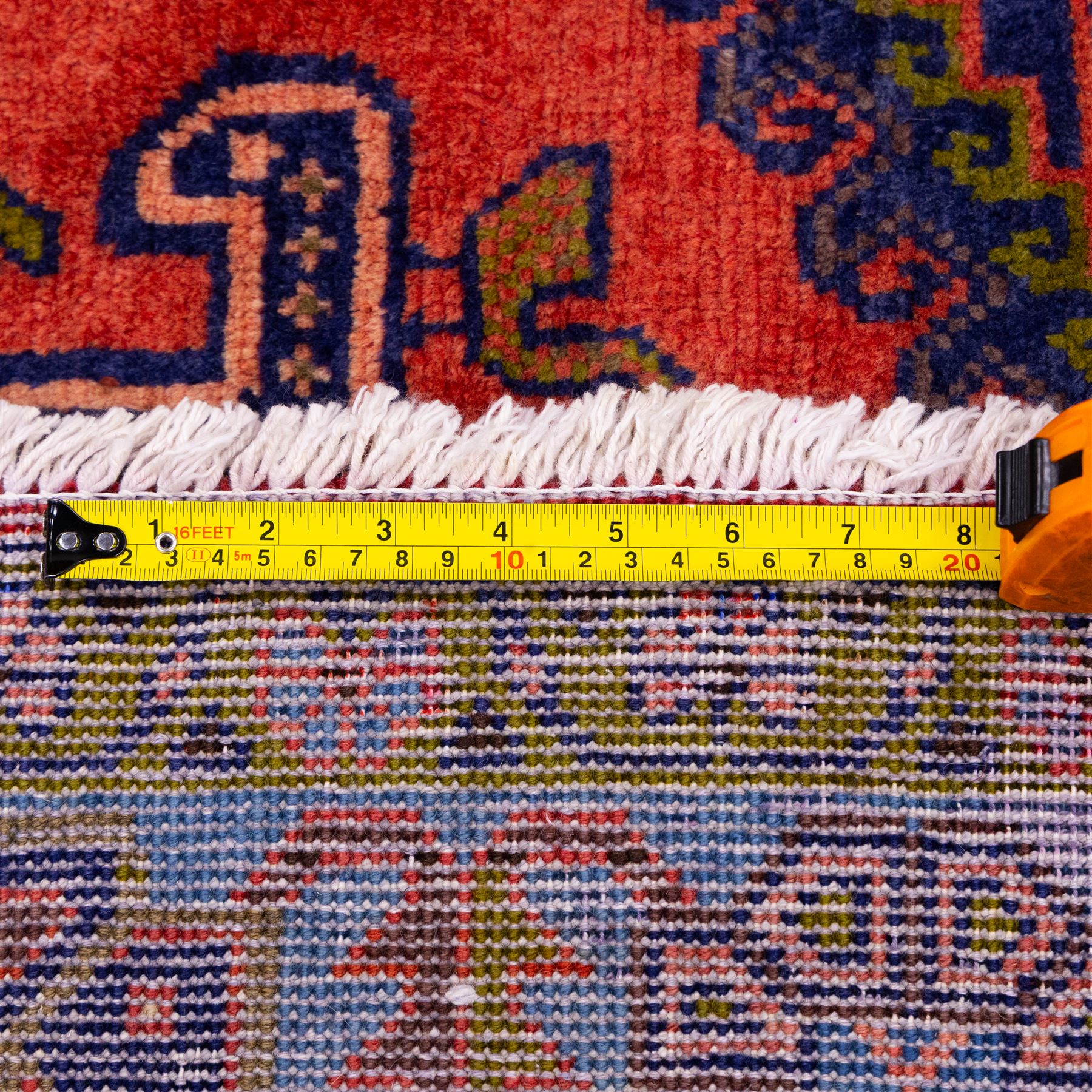 West Persian Veis hand-knotted rug, coral red field decorated with a series of bold geometric lozenge medallions in shades of indigo and sky blue surrounded by angular tribal motifs and stylized animal and plant forms framed by a deep indigo border of geometric ornament and multiple guard stripes, cotton fringe ends 