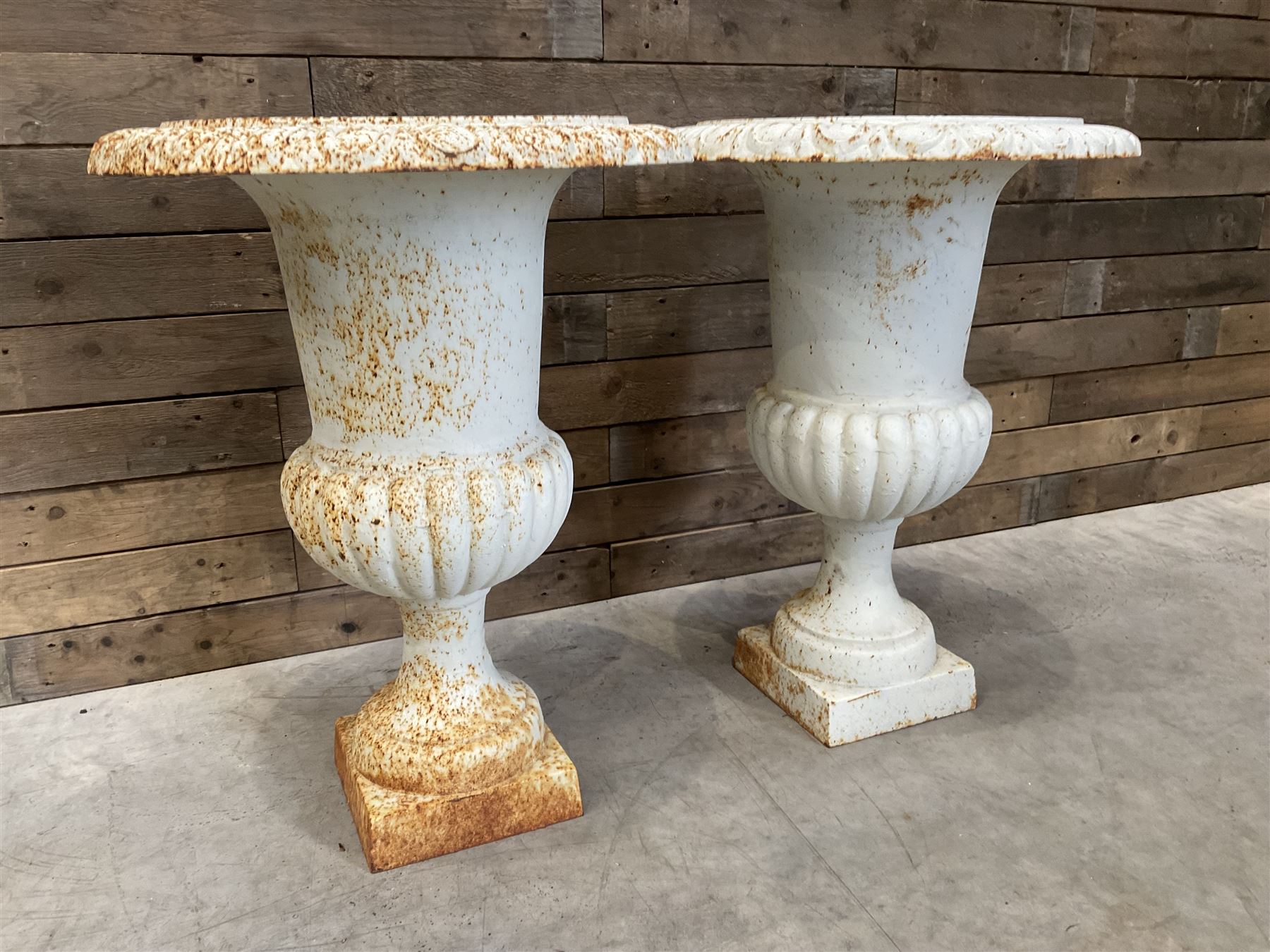 Pair of large Victorian design white painted cast iron campana shaped garden urns, egg and dart rim over a gadrooned underlobe, tapering column on square plinth base