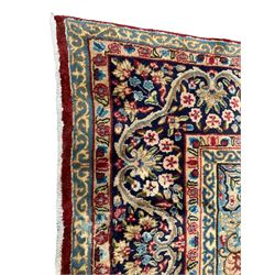 Persian Kirman crimson ground carpet, the field decorated with central floral medallion on a plain field decorated with flower head clusters, the outer field decorated with blue flower heads and stylised plant motifs, overall floral design border with trailing foliage branches, within guard bands 