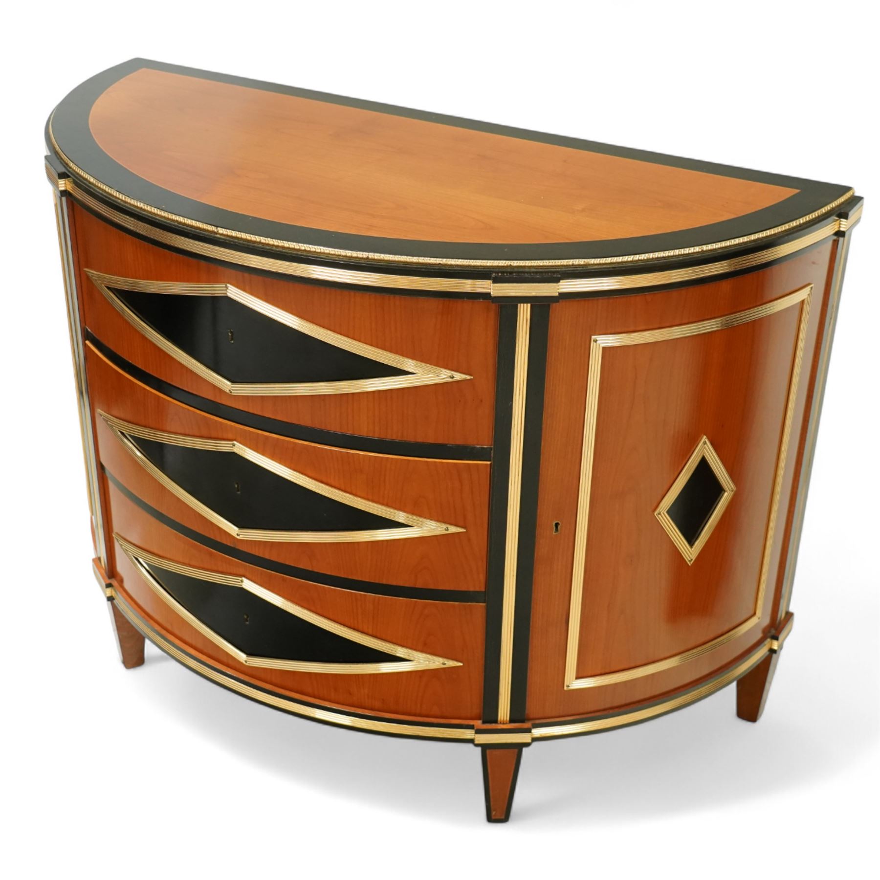 Colombo Mobili - Pair of Italian designer cherrywood art-deco inspired demi-lune commode cabinets, the shaped top with ebonised inlay and gilt brass repeating anthemion beading above a gilt brass reeded moulding, over three long drawers with gilt brass geometric panel mounts, flanked by cupboard doors with diamond motif, raised on tapering square supports 