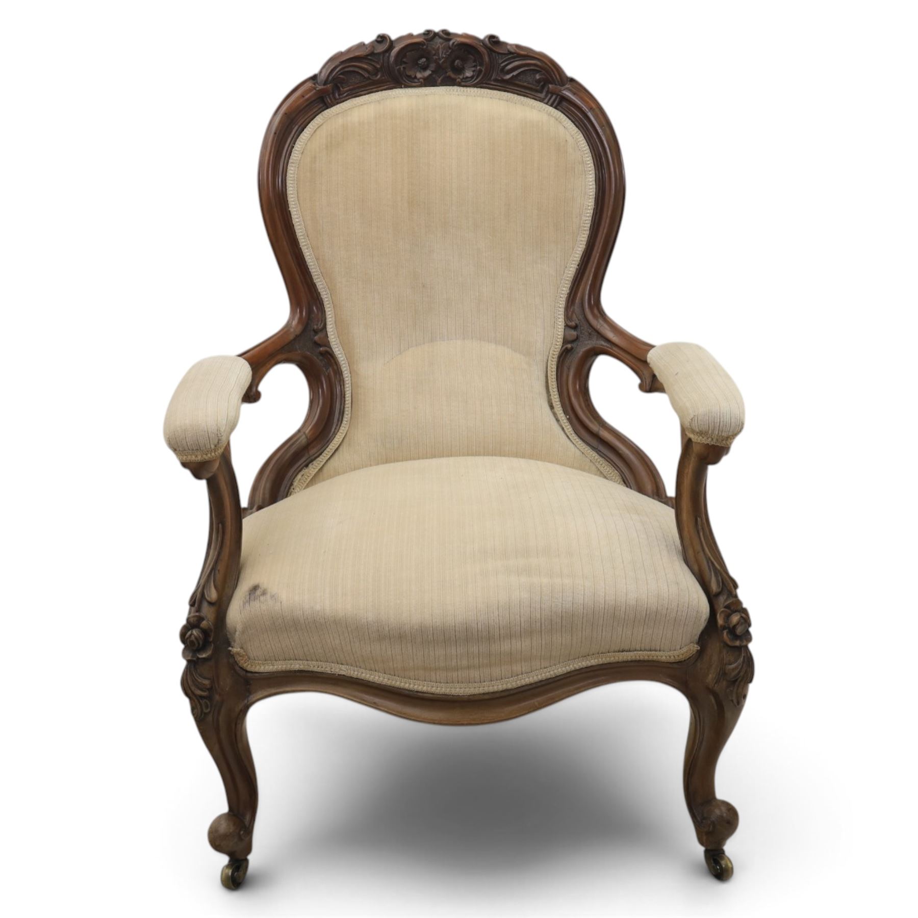Late Victorian walnut open armchair, the carved shaped cresting rail centred by scrolls and foliage above a padded serpentine back and overstuffed seat upholstered in cream striped fabric, with padded scroll arms on open carved supports, raised on cabriole supports with carved knees and ceramic castors
