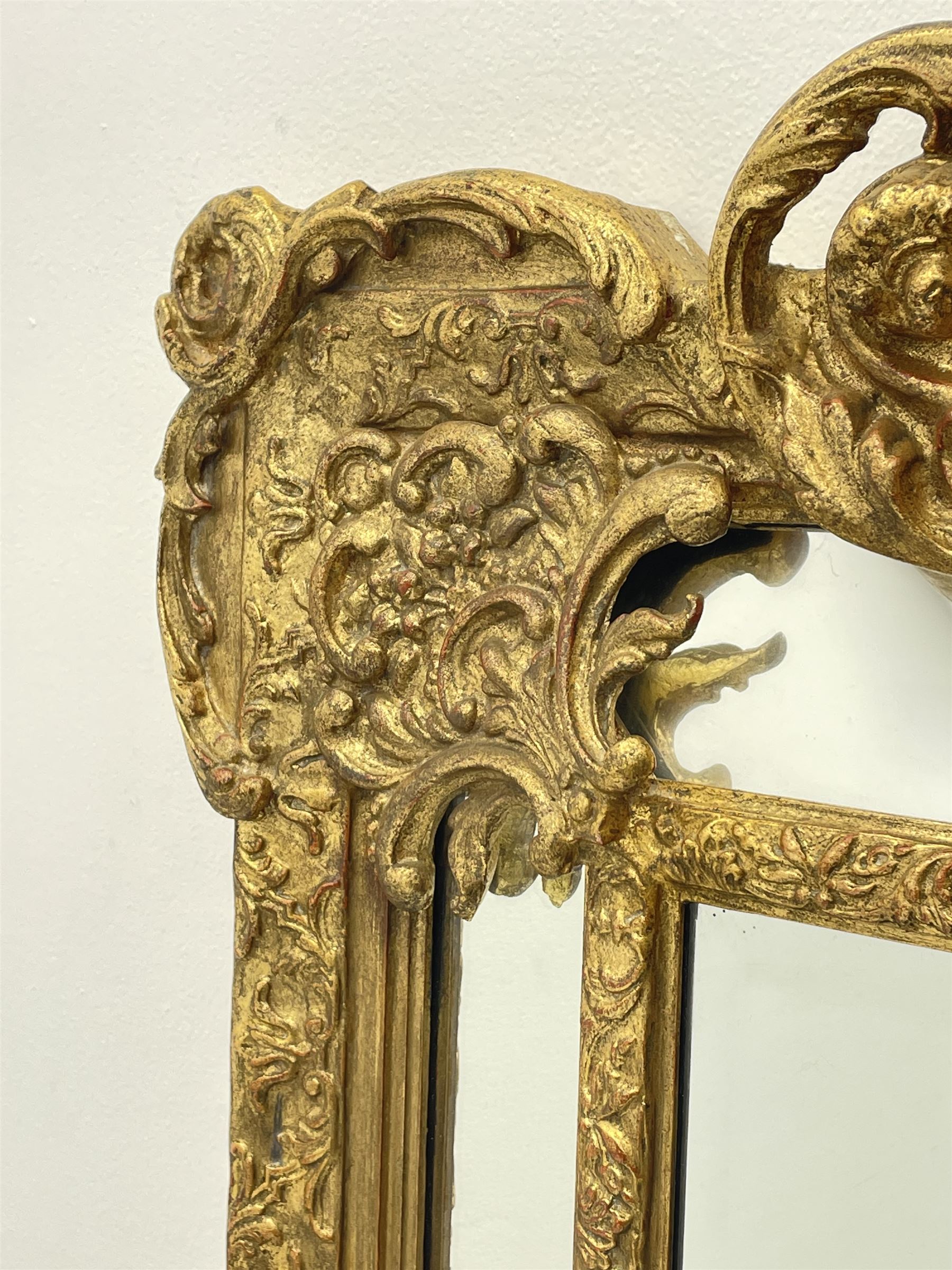 Large Victorian style gilt cushion framed mirror, putti holding urn with scrolled foliage pediment above central rectangular bevelled plate, the frame decorated with moulded foliate, each corner set with ornate cartouche