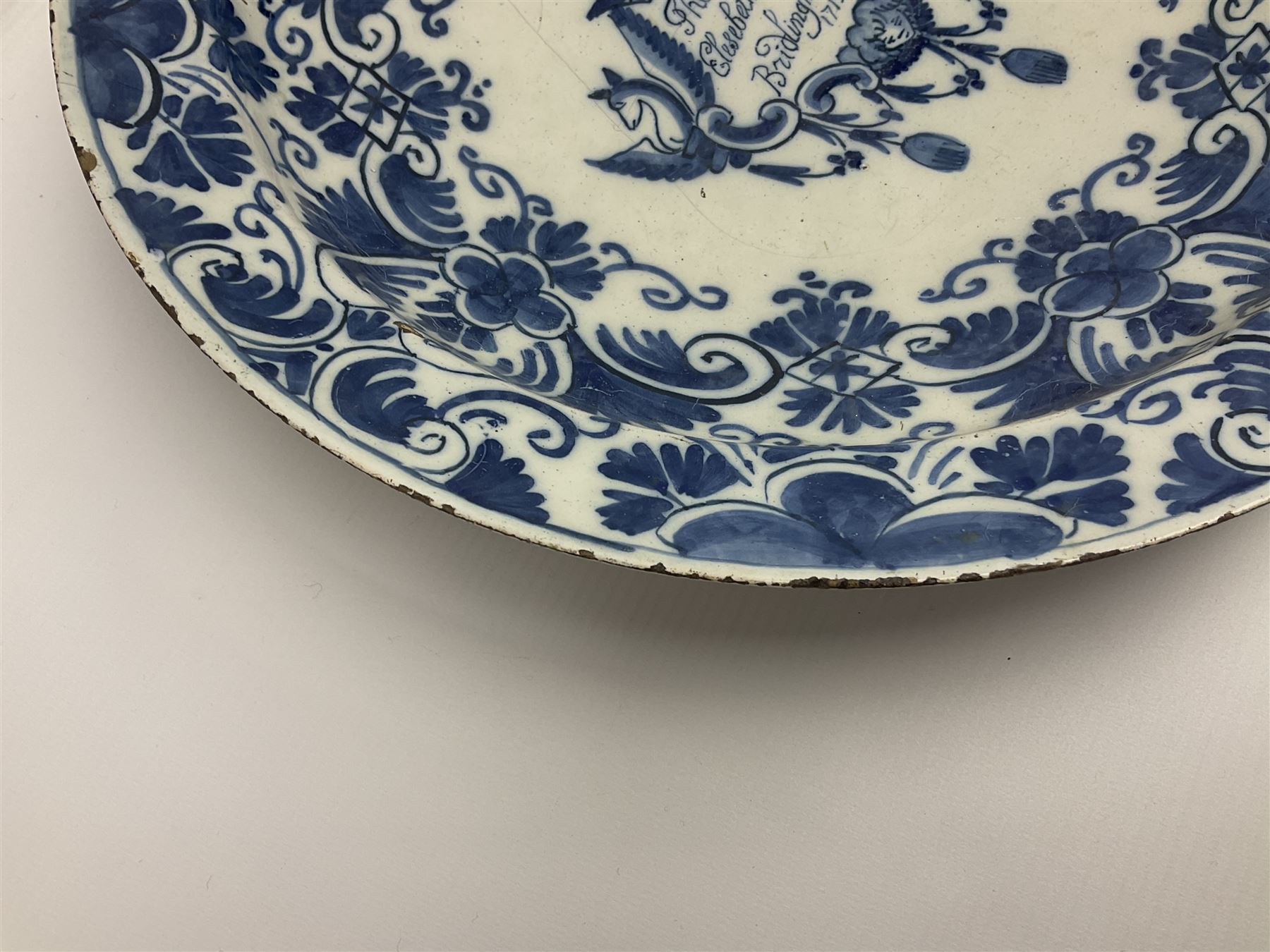 Early 18th century Delft marriage plate, of circular form with dished centre, the centre inscribed and dated 'Thomas and Elizabeth Kockerill Bridlington Key 1715' within a crowned C scroll cartouche, flanked by demi-griffins, above a putto head and tassels, within a wide foliate border, D34cm
