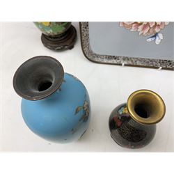 Six cloisonné vases, to include two pairs decorated with peonies and foliage on patterned gilt ground, all with carved hardwood stands, another of slender ovoid form decorated with birds upon blossoming branches on vibrant blue ground, etc, together with a square cloisonné tray, L17.5cm