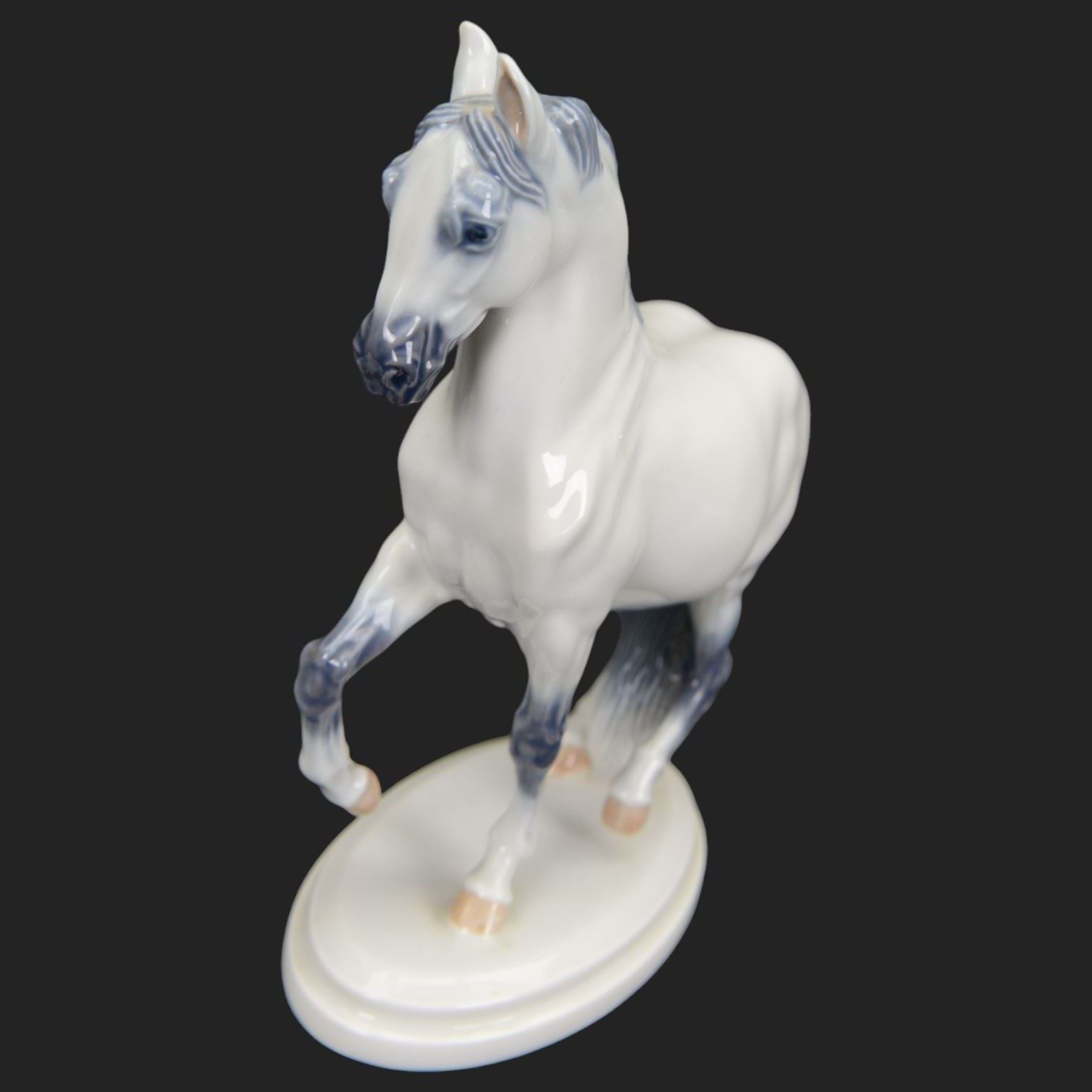 Two Royal Copenhagen figures modelled as Lippizaner horses, the first example in a recumbent pose no 5690, the second example prancing upon a stepped circular base, H19cm 