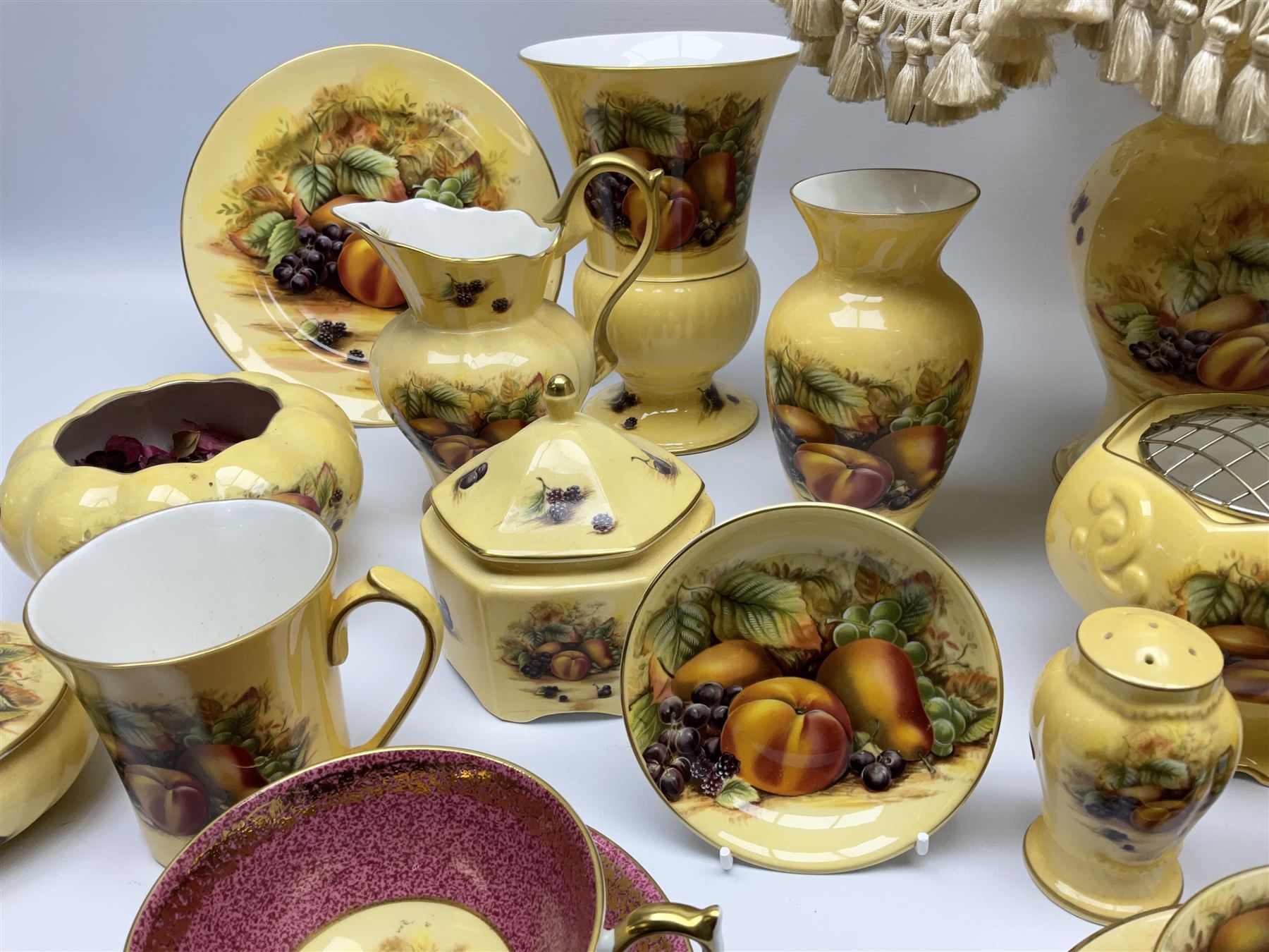 Collection of Aynsley Orchard Gold pattern wares, comprising lamp base, three jars and covers, six vases or various size and form, large jug, lidded dish, pair of cruets, pair of candlesticks, mug, two pin dishes, lobed dish, tea cup, saucer, size plate, and cake plate, and two further cups and saucers, each cup decorated with central Orchard Gold reserve to the interior against a mottled pink or green ground. 