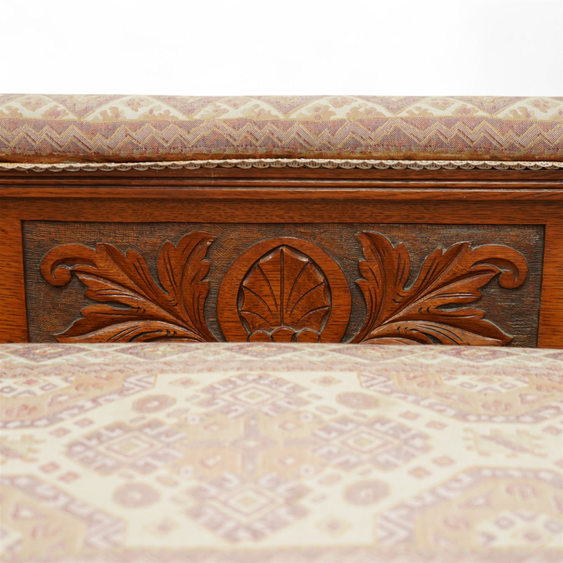 Late Victorian walnut chaise longue, upholstered in geometric patterned fabric, the scroll end and padded back above carved side panel with foliate and roundel motifs, shaped seat rail on turned front supports with ceramic castors
