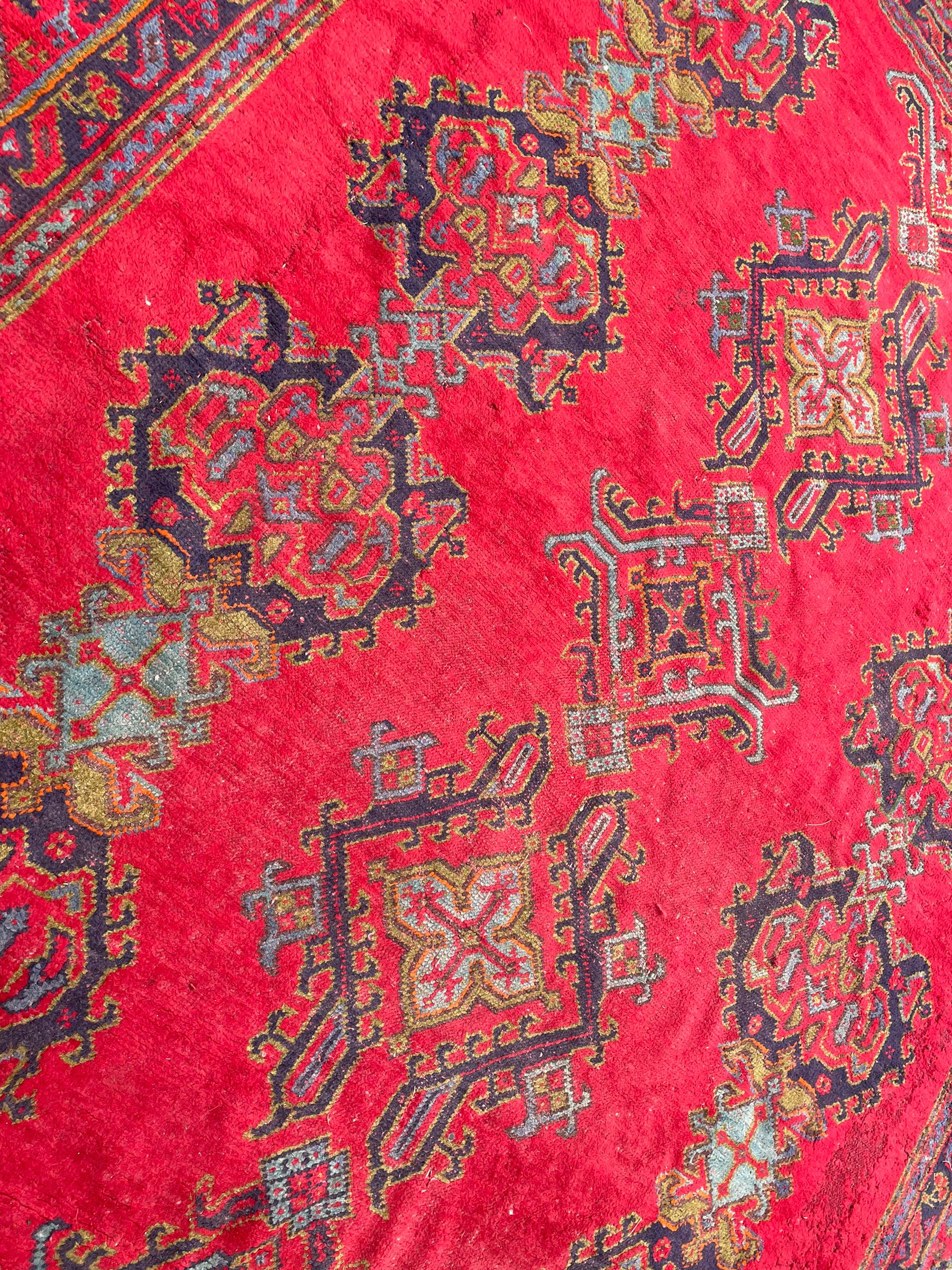 Early 20th century Western Anatolia Turkish Oushak crimson ground carpet, the field decorated with rows of Herati and Palmette medallions, the main border decorated with stylised flower head motifs within guard stripes
