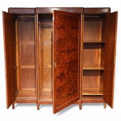 Early 20th century French burr maple breakfront armoire, enclosed by three panelled doors with bookmatched veneer and stringing, outer doors inlaid with gilt urn medallions, fitted interior with hanging spaces flanking a shelved compartment, raised on short tapered legs