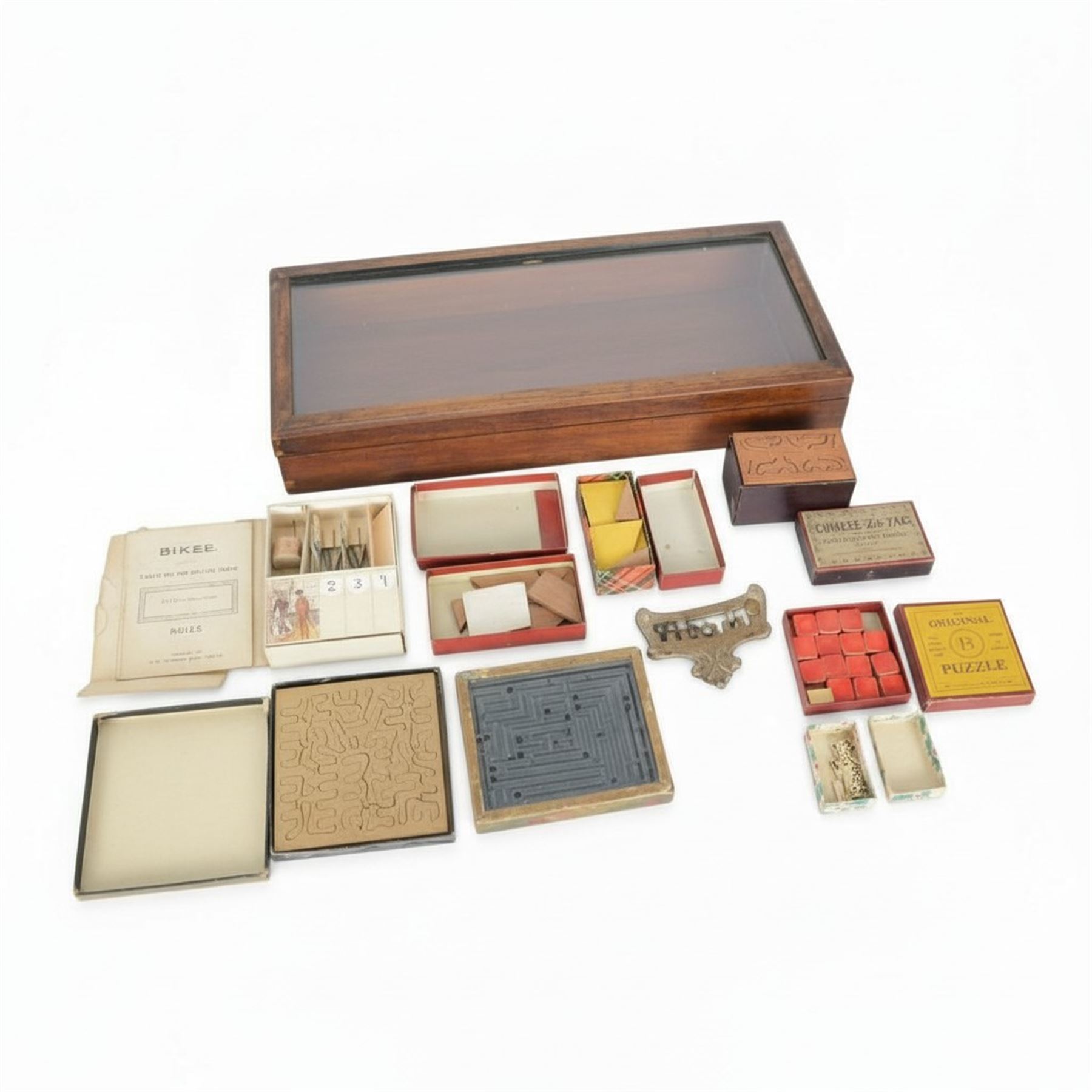 Early 20th century and later puzzles and games, including Bikee, 'A Novel and Very Amusing Game', by C.W. Faulkner & Co, Multum-In-Parvo Puzzle by RJ London, The Original 15 Puzzle by RJ London, The Chinese Zig-Zag 'A Wonderful and Extraordinary Puzzle', The Subway Puzzle by R Journet London, etc, all in glazed wooden display case