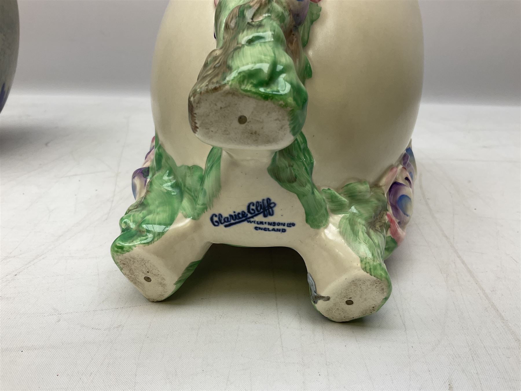 1930s Carlton Ware Art Deco Garden pattern vase of shouldered ovoid form, decorated with blue, pink and yellow flower heads on a mottled blue and white ground, pattern no. 3413, with printed and painted marks beneath, H19cm, together with a Clarice Cliff My Garden pattern vase, raised upon three feet with blue, pink and purple moulded Hollyhock design, H20cm, with Clarice Cliff Wilkinson Ltd England marks beneath