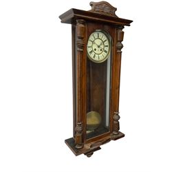 German spring driven wall clock c 1910, with an eight day Gustav Becker movement striking the hours on a coiled gong, in a walnut case with a flat top and carved pediment, fully glazed door flanked by turned columns, two part enamel dial with roman numerals, gothic hands and spun brass bezel, with pendulum and beat plate.