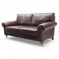 Laura Ashley - brown leather two seater sofa, loose cushion back and seat, flanked by scrolled arms upon light stained wood supports on castors