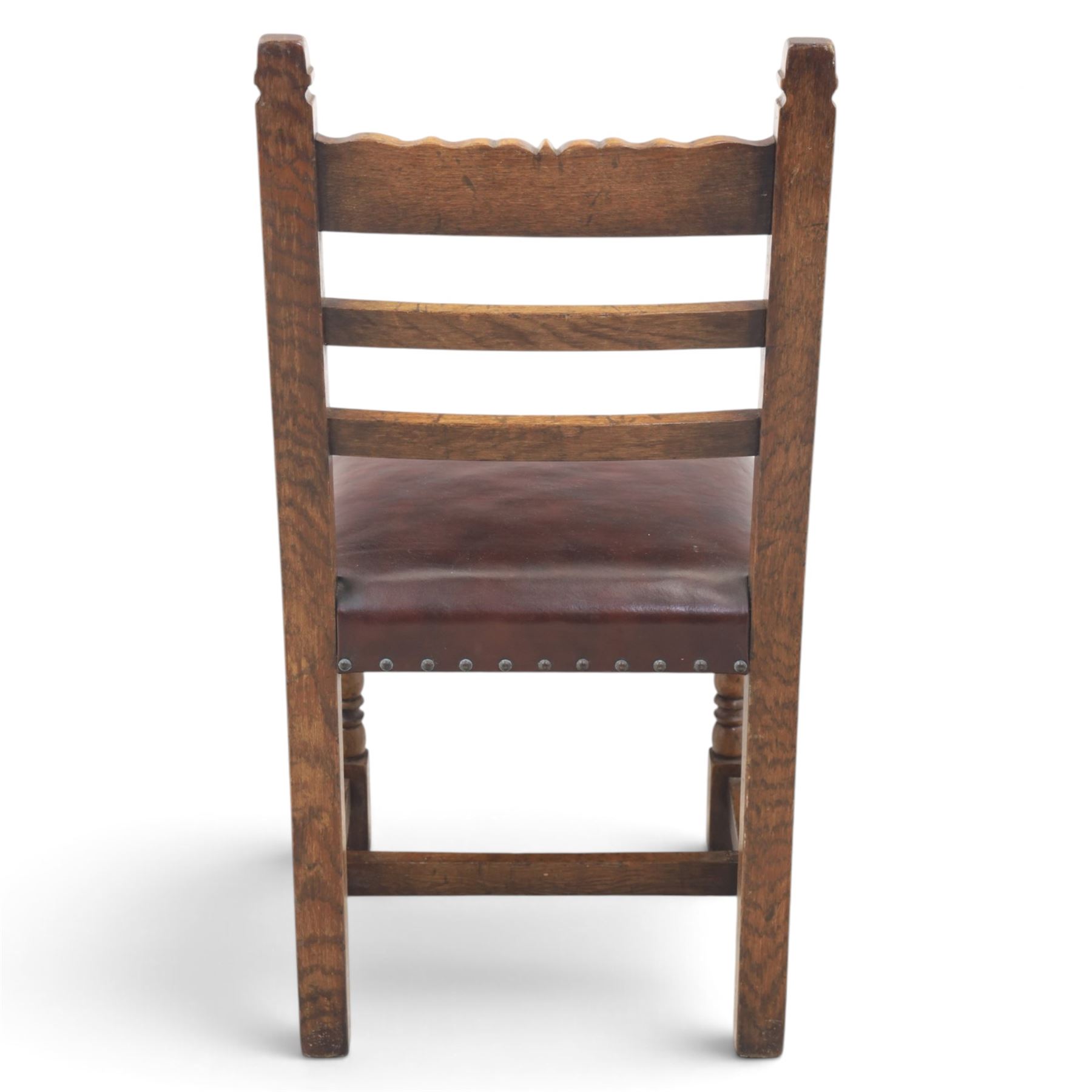 Craftsman made set of four solid oak dining chairs with leather seats, with carved cresting rail, on red leather seats with studded trim, raised on block and turn supports united by H-stretcher