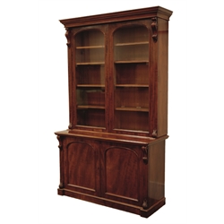  Victorian mahogany bookcase on cupboard, projecting cornice above two arched glazed doors, carved scrolled corbels, the base with panelled cupboard on a skirted base, W141cm, H227cm, D55cm  