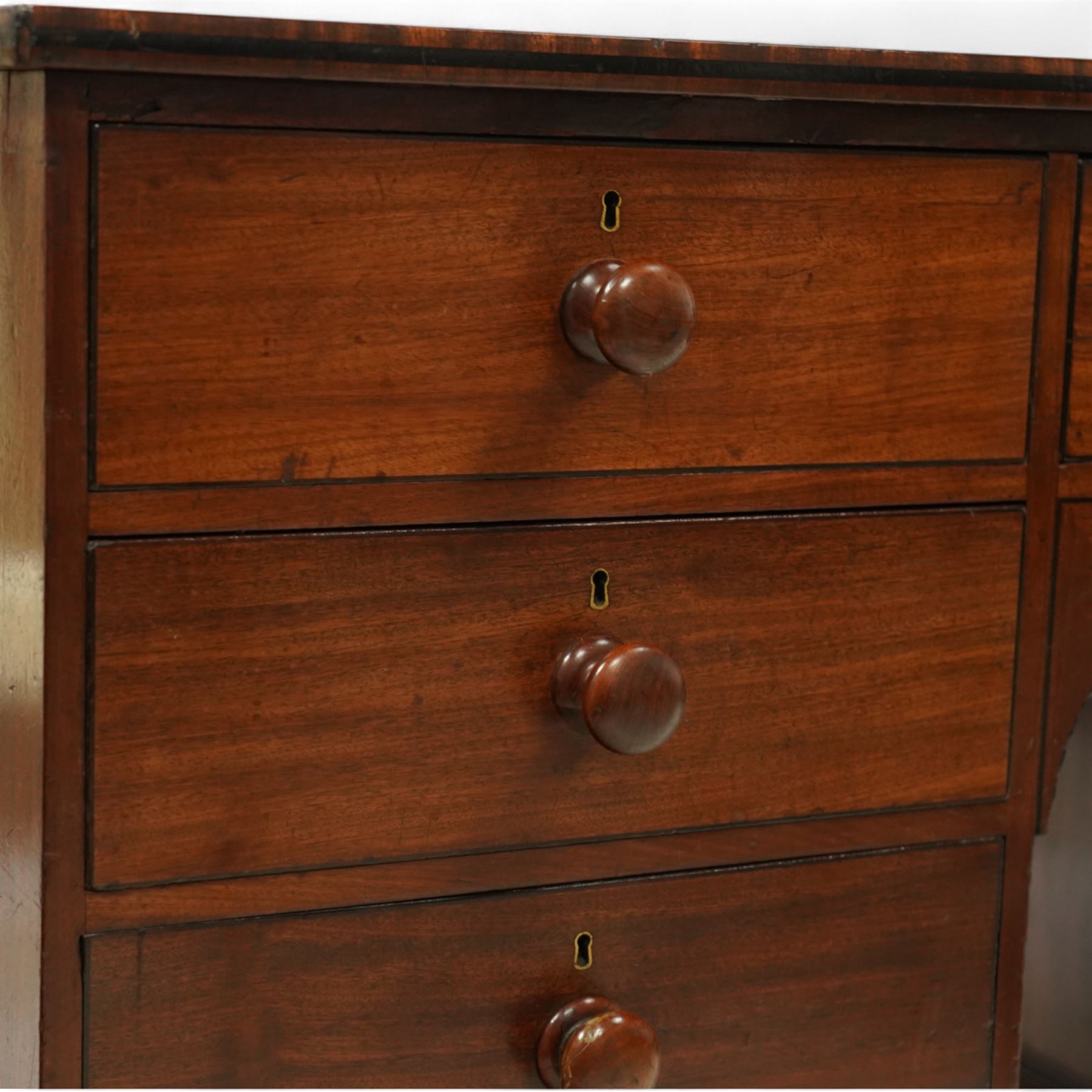 Early 19th century mahogany kneehole desk, rectangular moulded top over an arrangement of nine drawers with turned mahogany handles, arched kneehole recess, raised on short turned legs with brass cups and castors