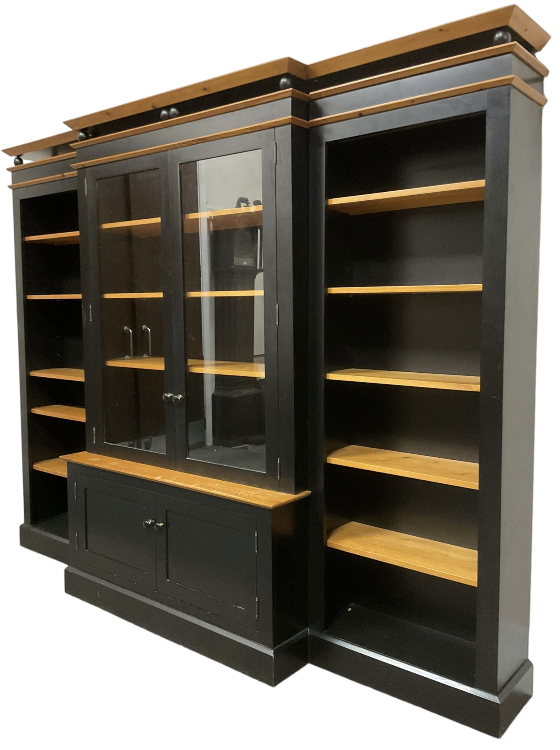 Contemporary polished pine and black finish break-front bookcase, projecting cornice over globular mounts, central cabinet enclosed by two glazed doors over double panelled cupboard, flanked by adjustable shelves, on plinth base