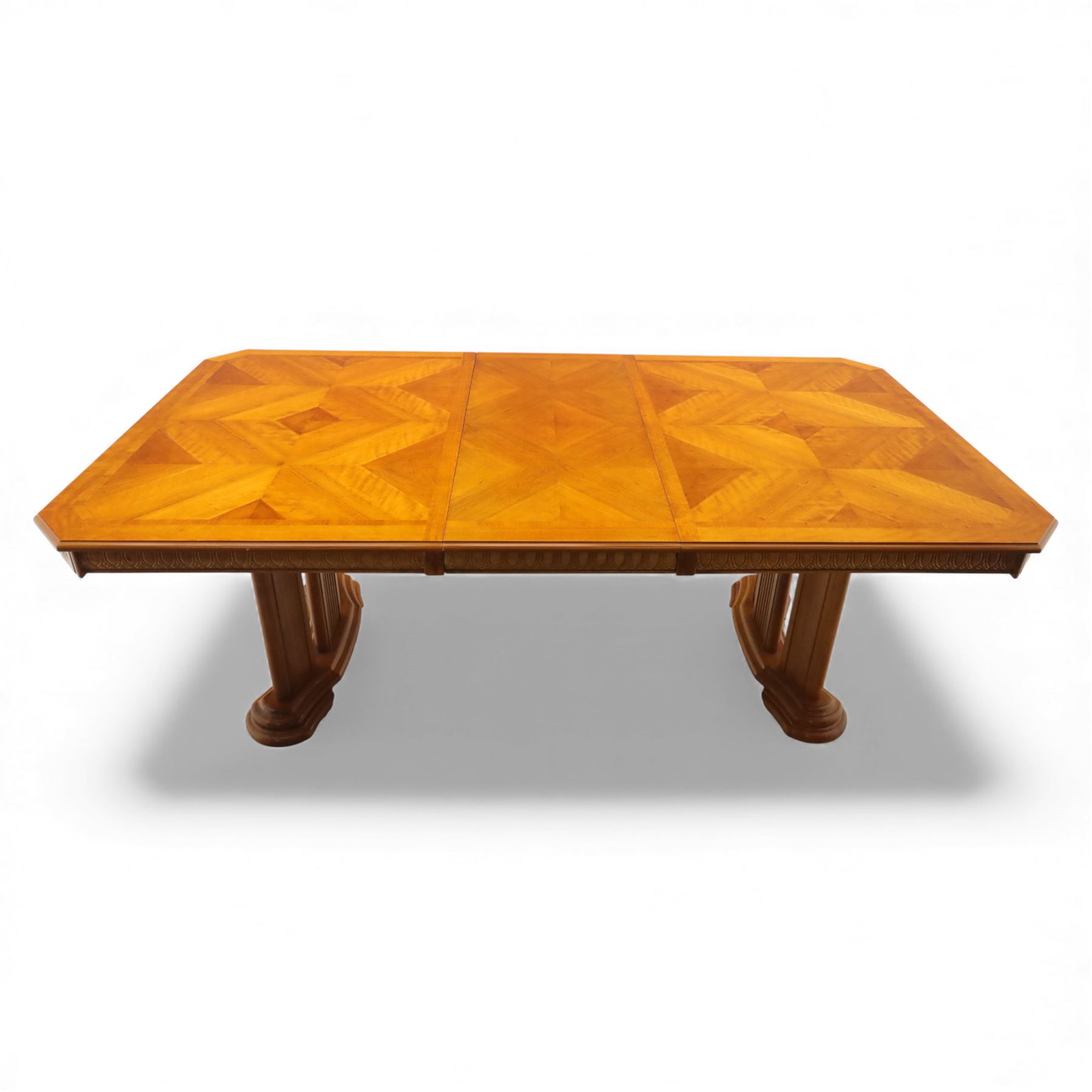 Late 20th century parquetry veneered extending dining table and eight chairs, the rectangular top with canted corners decorated with geometric parquetry panels, moulded edge frieze with repeating carved detail, raised on twin pedestal supports with fluted columns and shaped platform bases, the chairs with pierced splat backs and upholstered drop-in seats
Extends on a central leaf to 208cm