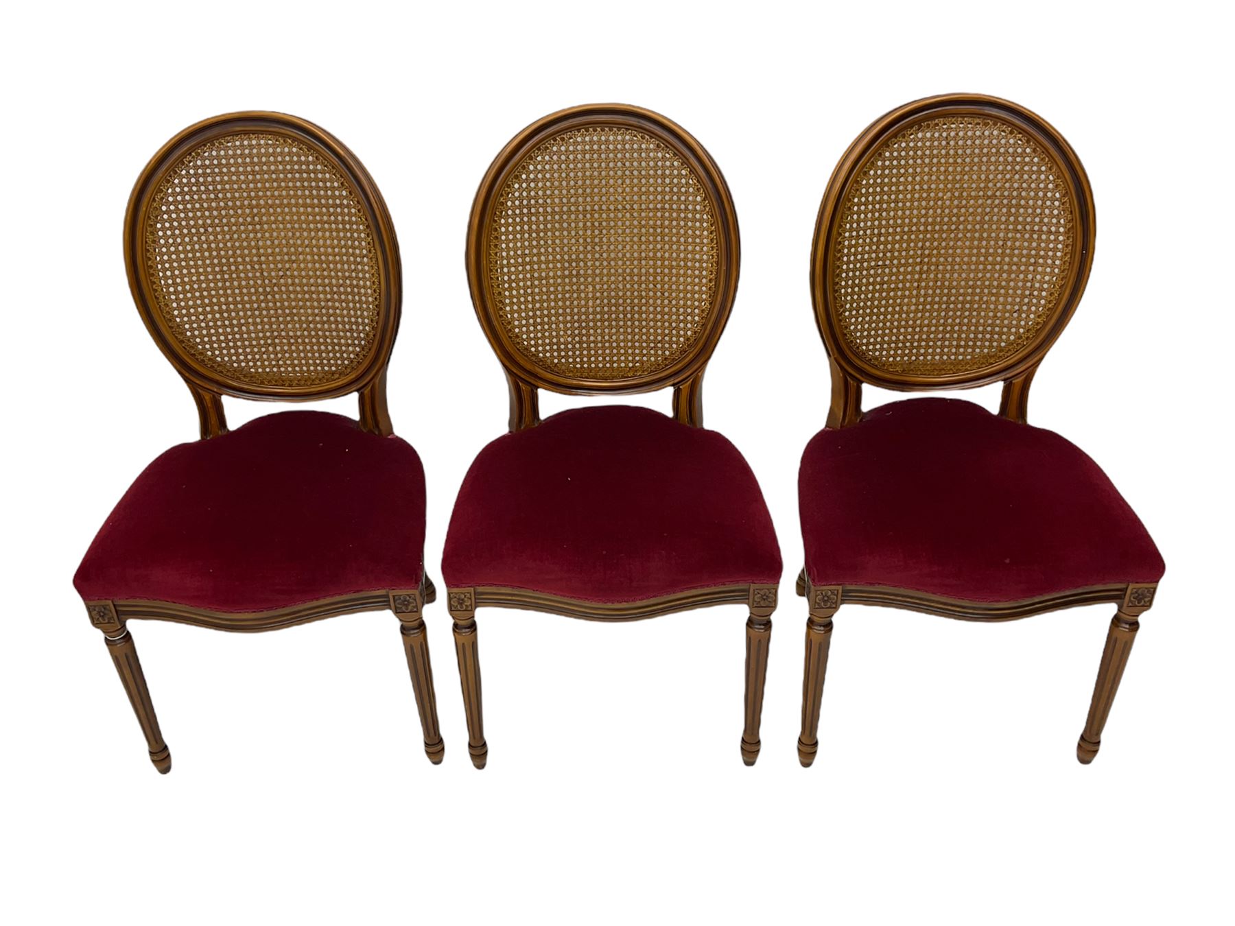 Set six French style walnut finish dining chairs, oval cane bergere backs over serpentine seats upholstered in red, flower head carved fluted supports