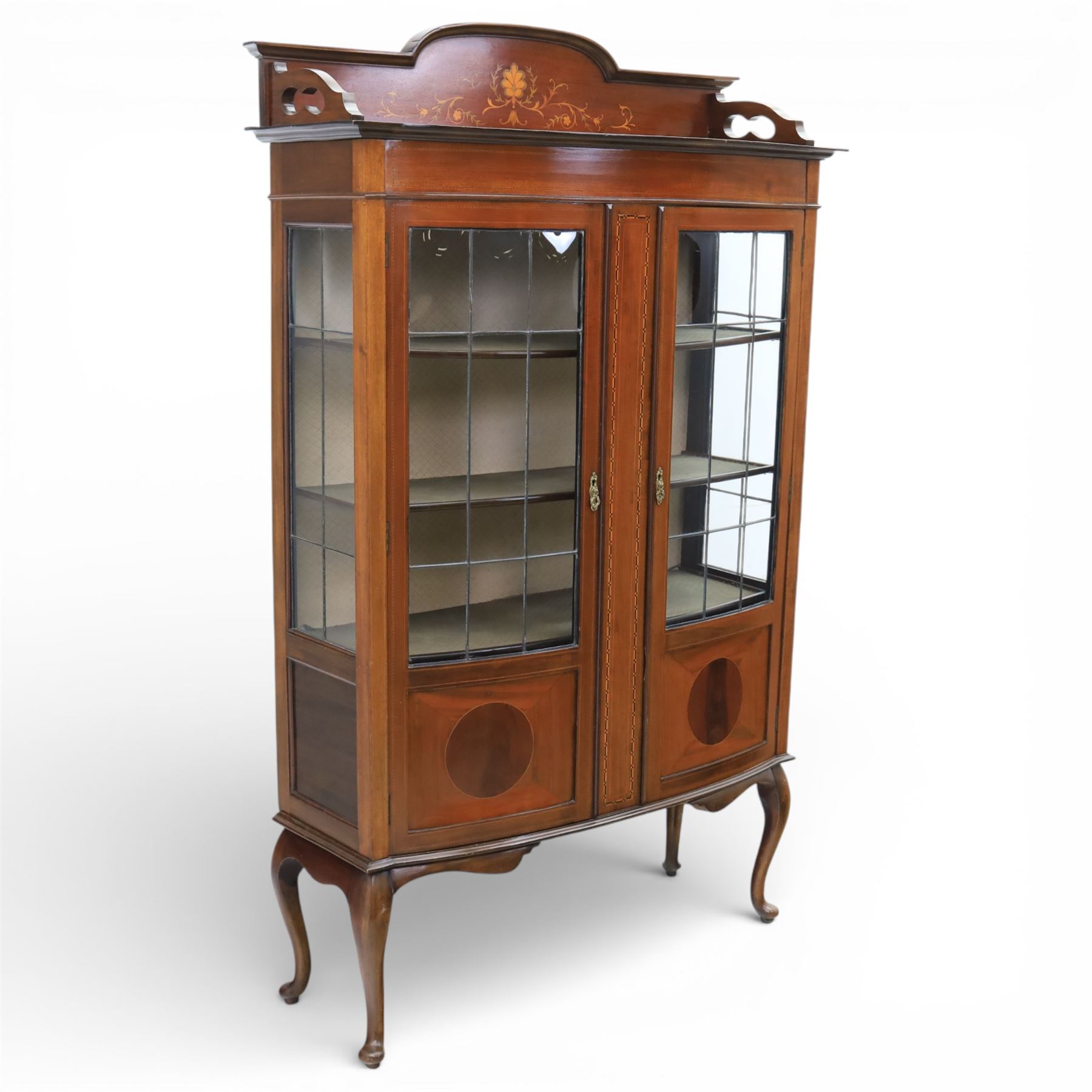 Edwardian mahogany display cabinet, arched back with satinwood and harewood marquetry foliate decoration above a moulded cornice, serpentine front fitted with twin glazed doors with astragal bars, the lower door panels inlaid with oval reserves, standing on elegant cabriole legs terminating in pad feet
