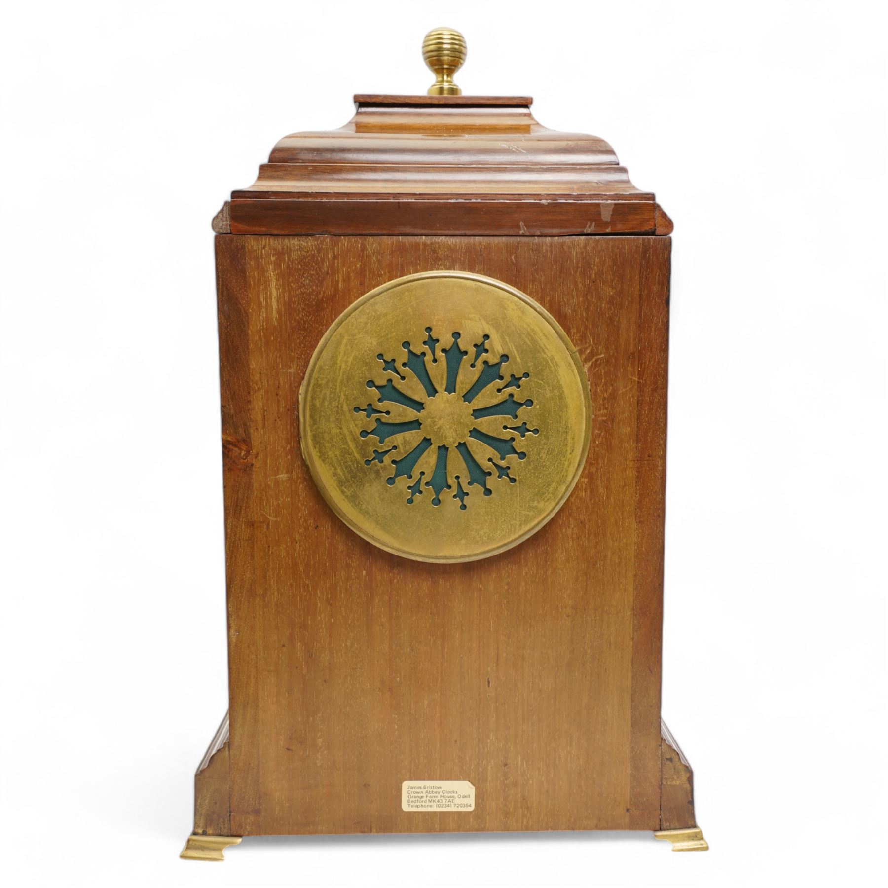 Edwardian- Early 20th century 8-day mahogany mantle clock, with a stepped pediment and brass finial, recessed brass pilasters and brass inlay to the front with a conforming plinth raised on bracket feet, silvered dial with Arabic numerals and steel spade hands within a glazed brass bezel, single train timepiece movement with pendulum and key.
